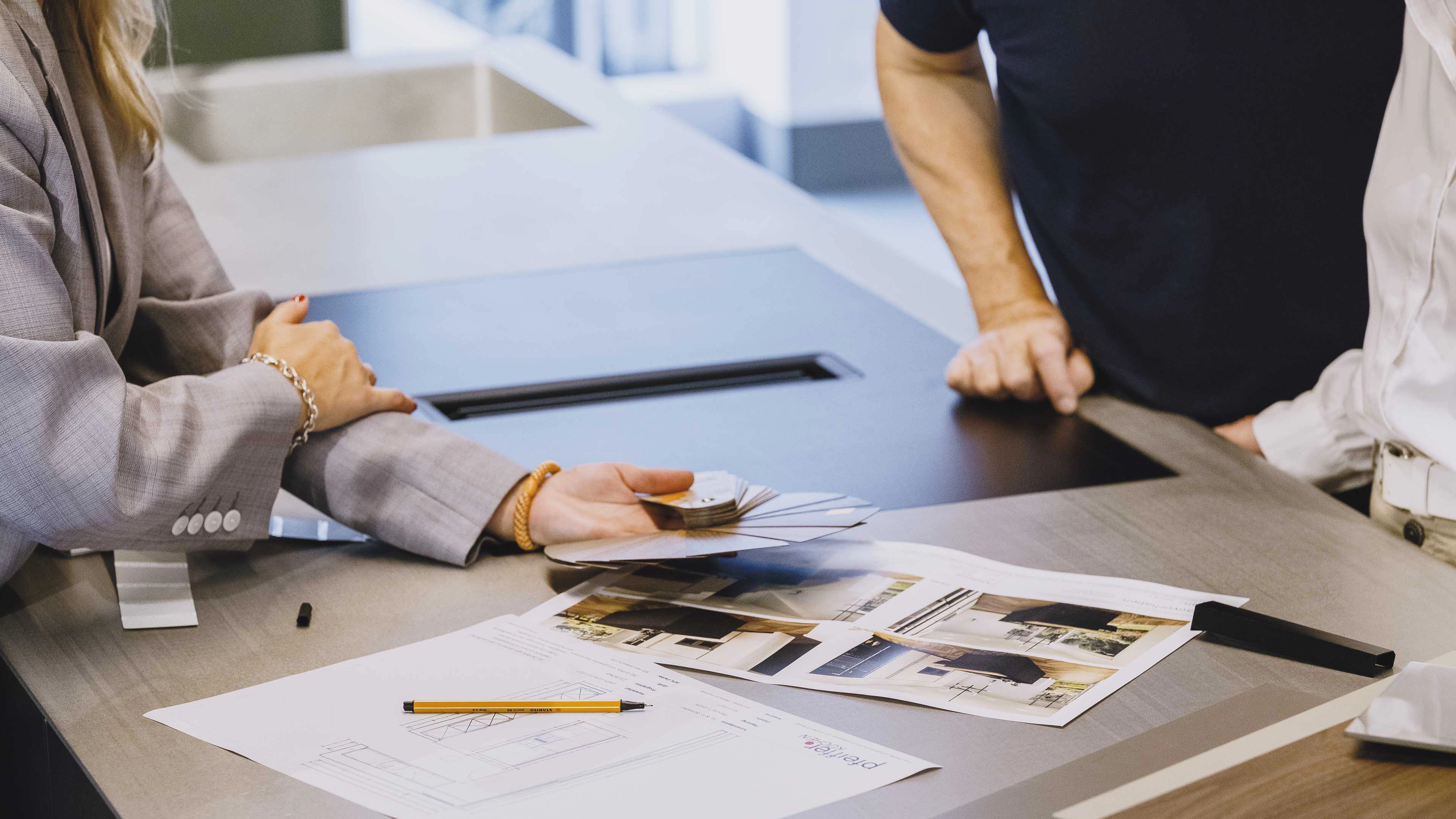 People discussing interior design samples and architectural plans on a table.