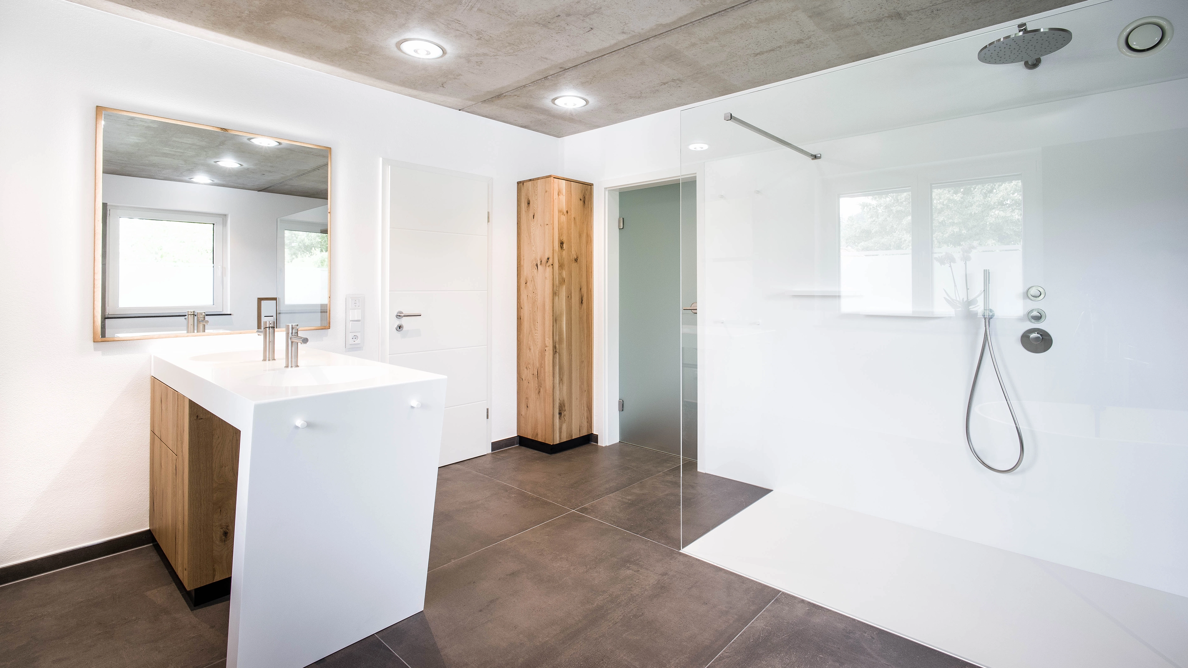 Modern bathroom with a large white vanity, wooden accents, and a walk-in shower with glass partition.