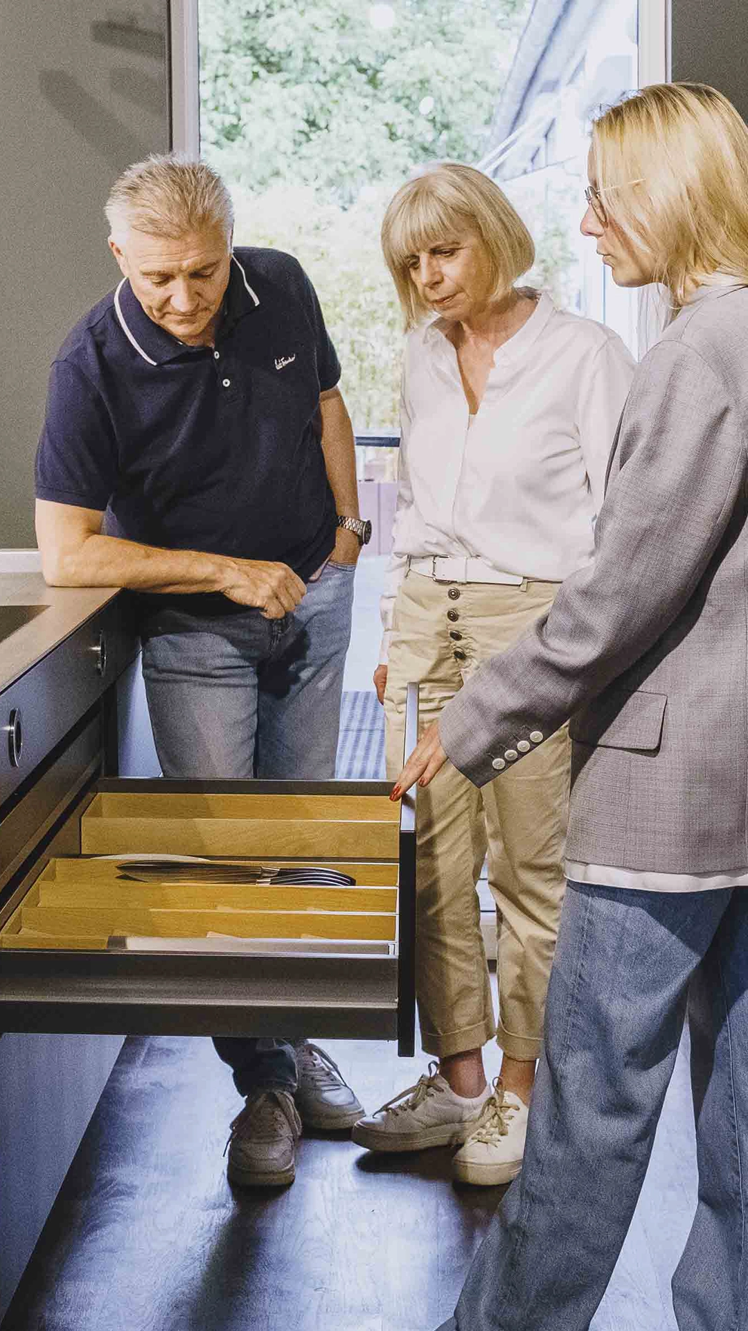 Three adults standing around an open kitchen drawer with cutlery organizers.