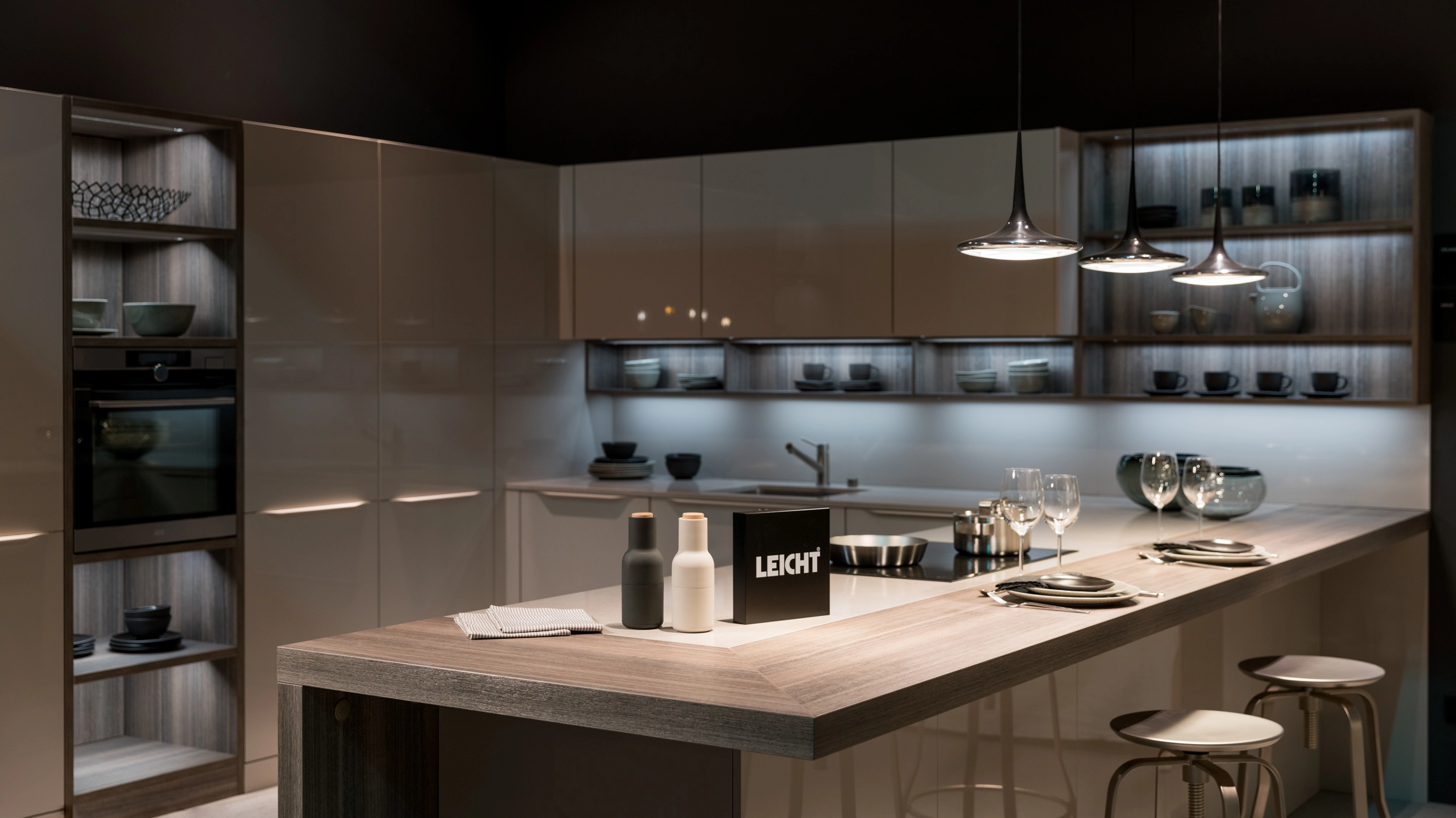 Modern kitchen with a wooden countertop island, three pendant lights, built-in oven, and illuminated shelves displaying dishes