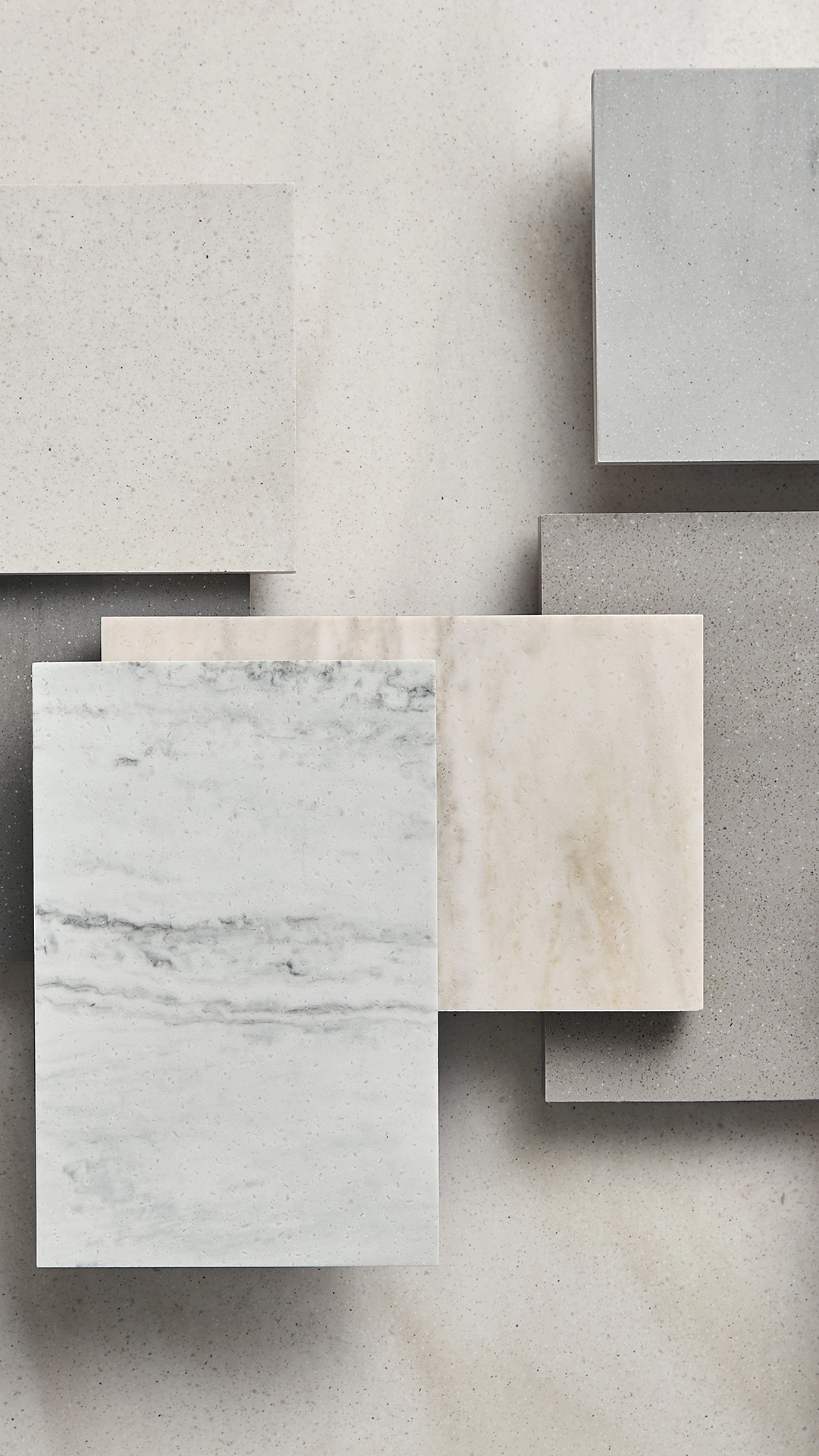 Overlapping square slabs of various neutral-toned materials including marble and textured surfaces arranged on a similarly textured background.