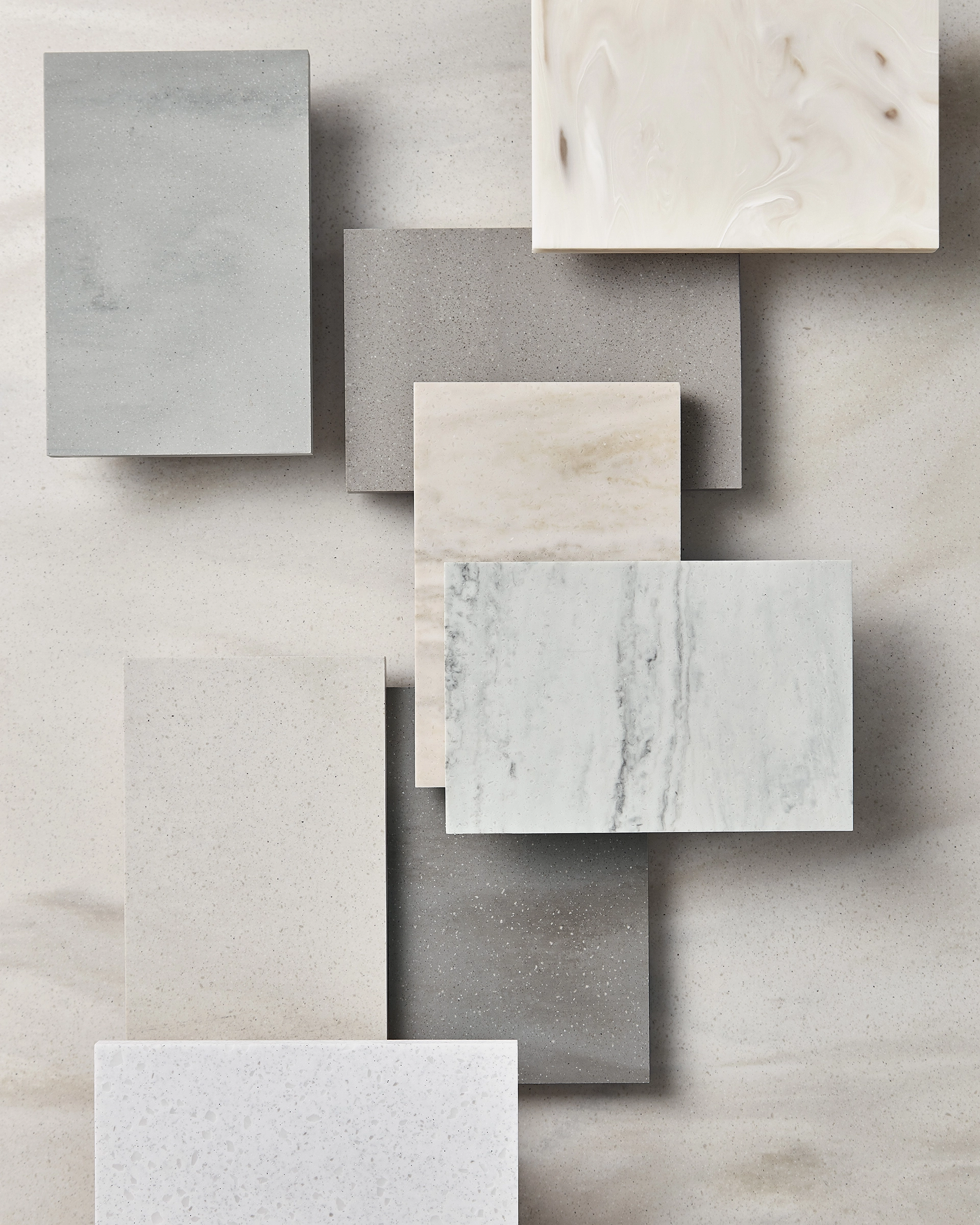 Arrangement of nine rectangular stone and marble samples in various neutral tones and patterns on a light beige surface.