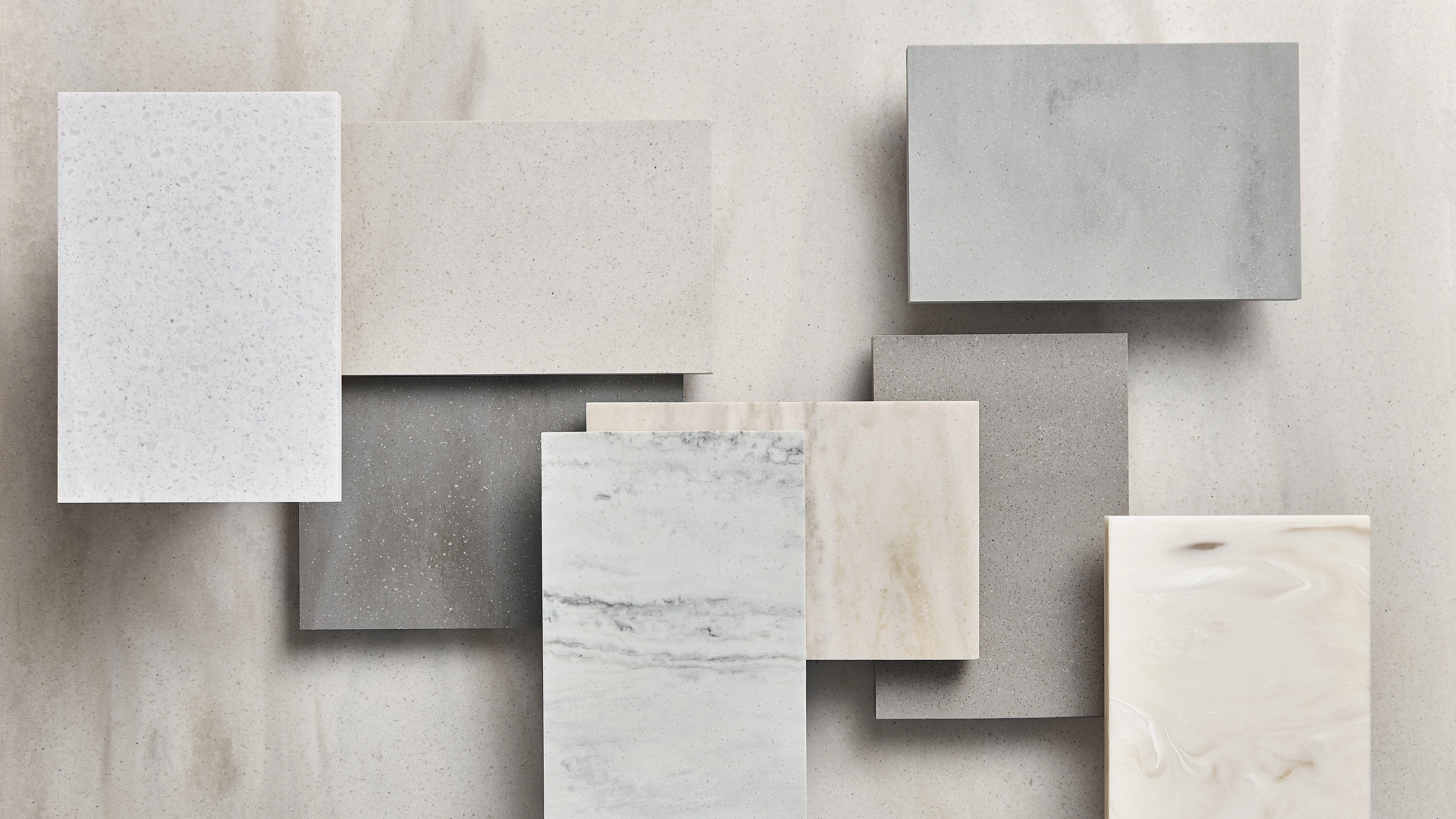 Assorted rectangular stone and marble slabs in neutral tones arranged on a light beige surface.