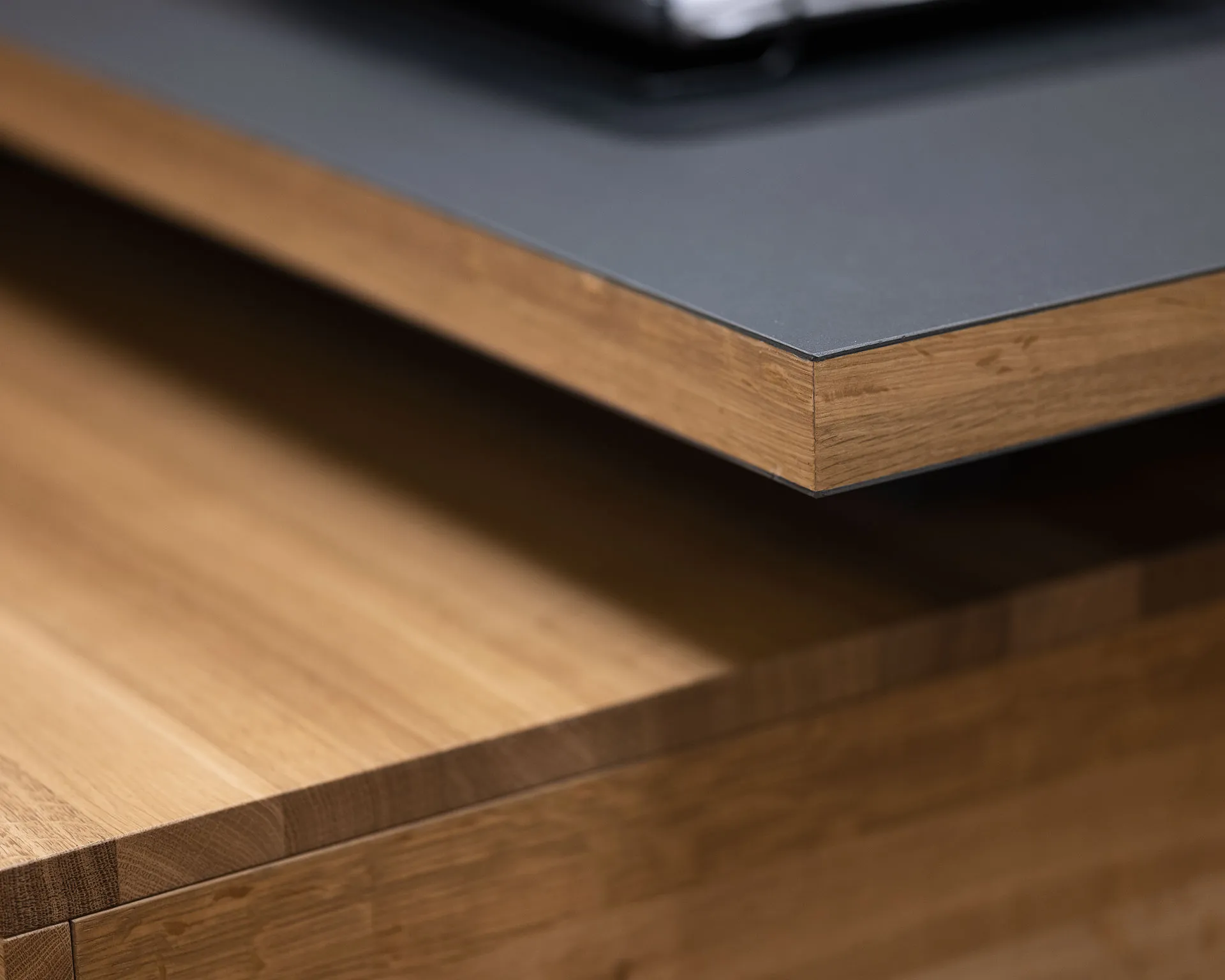 Close-up of a modern countertop with a dark gray surface and wooden edge over a wooden cabinet.