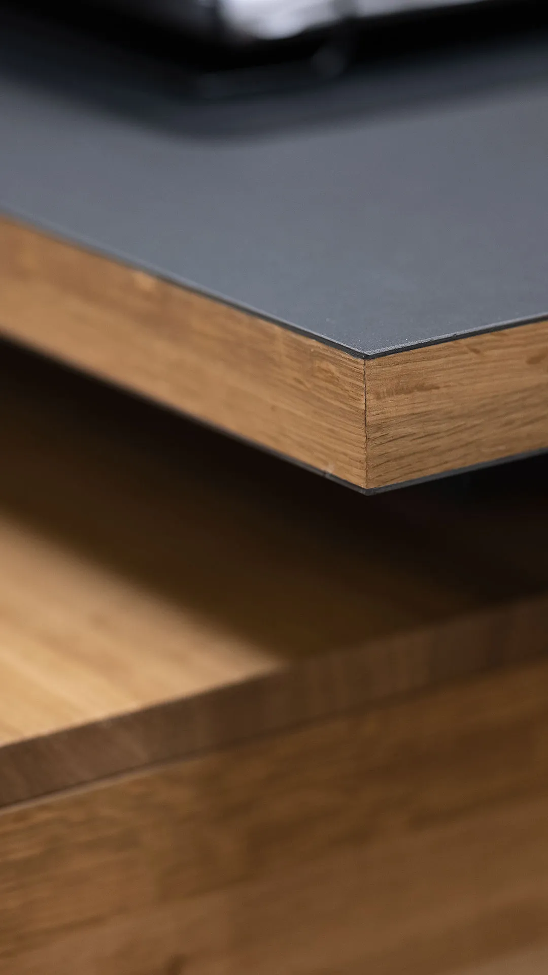 Close-up of a table or countertop with a black matte surface and wooden edge and base.