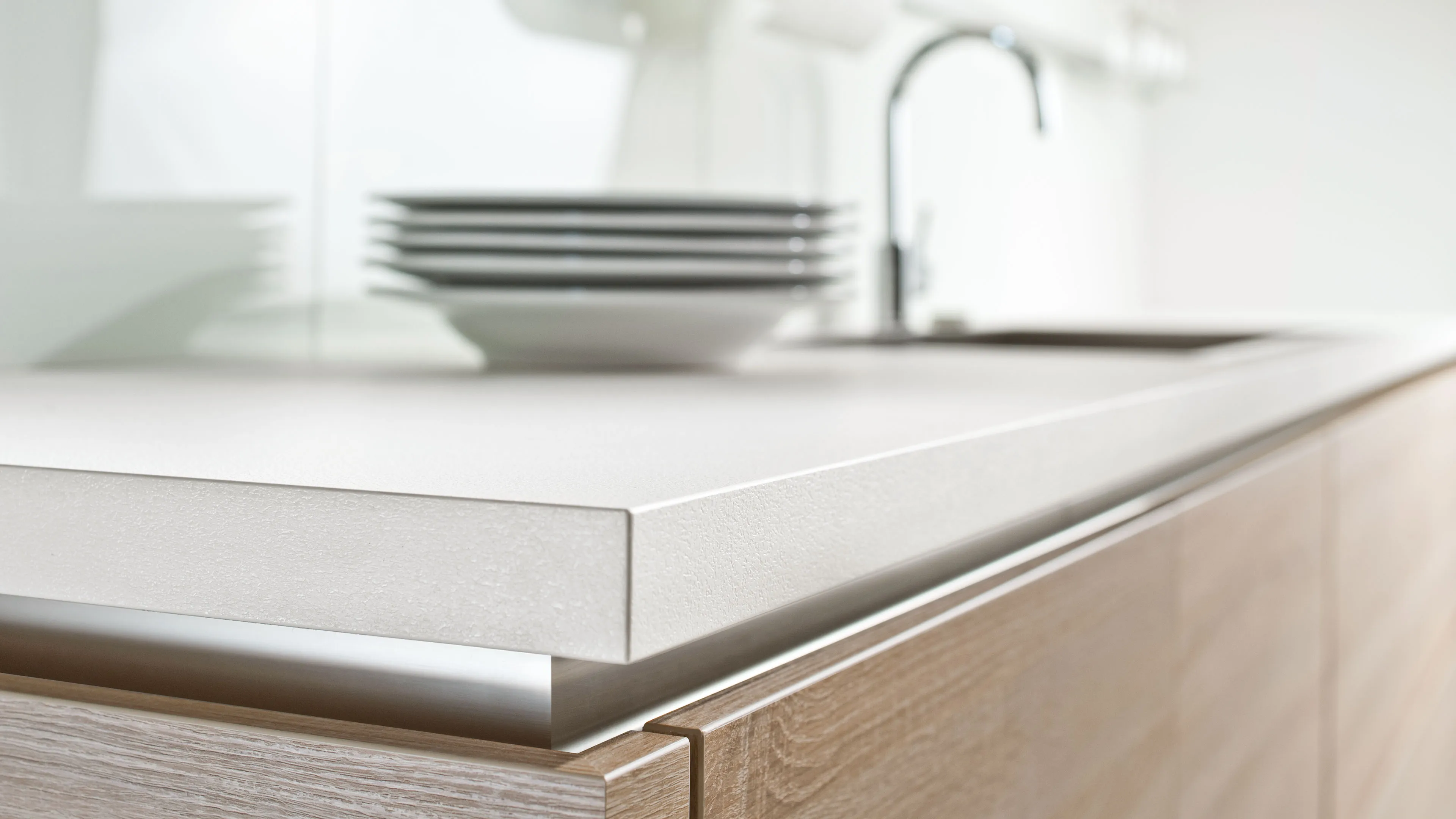 Close-up of a modern kitchen countertop with wooden cabinets and stacked white plates in the background.