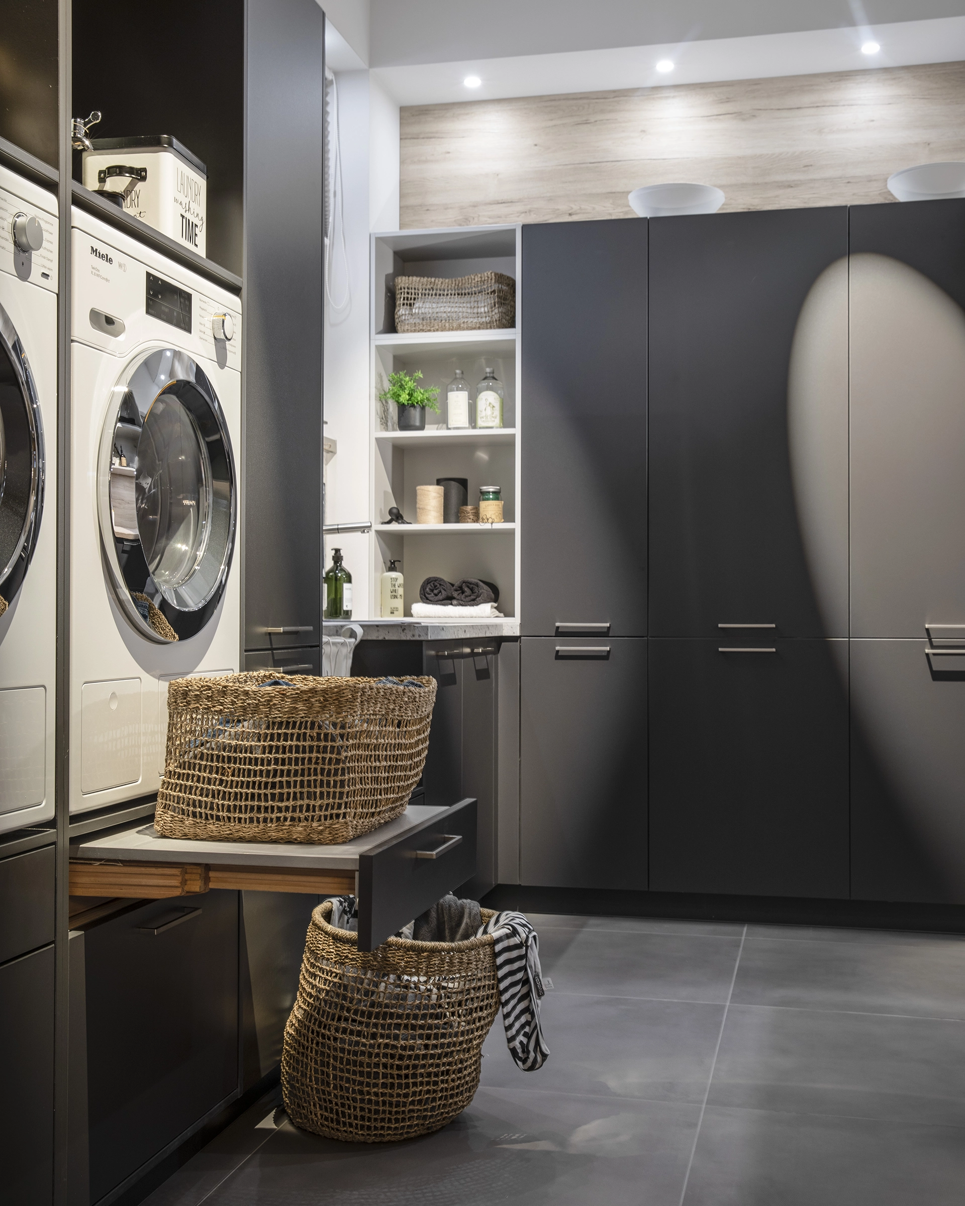 Modern laundry room with stacked washer and dryer, dark cabinets, and woven laundry baskets.
