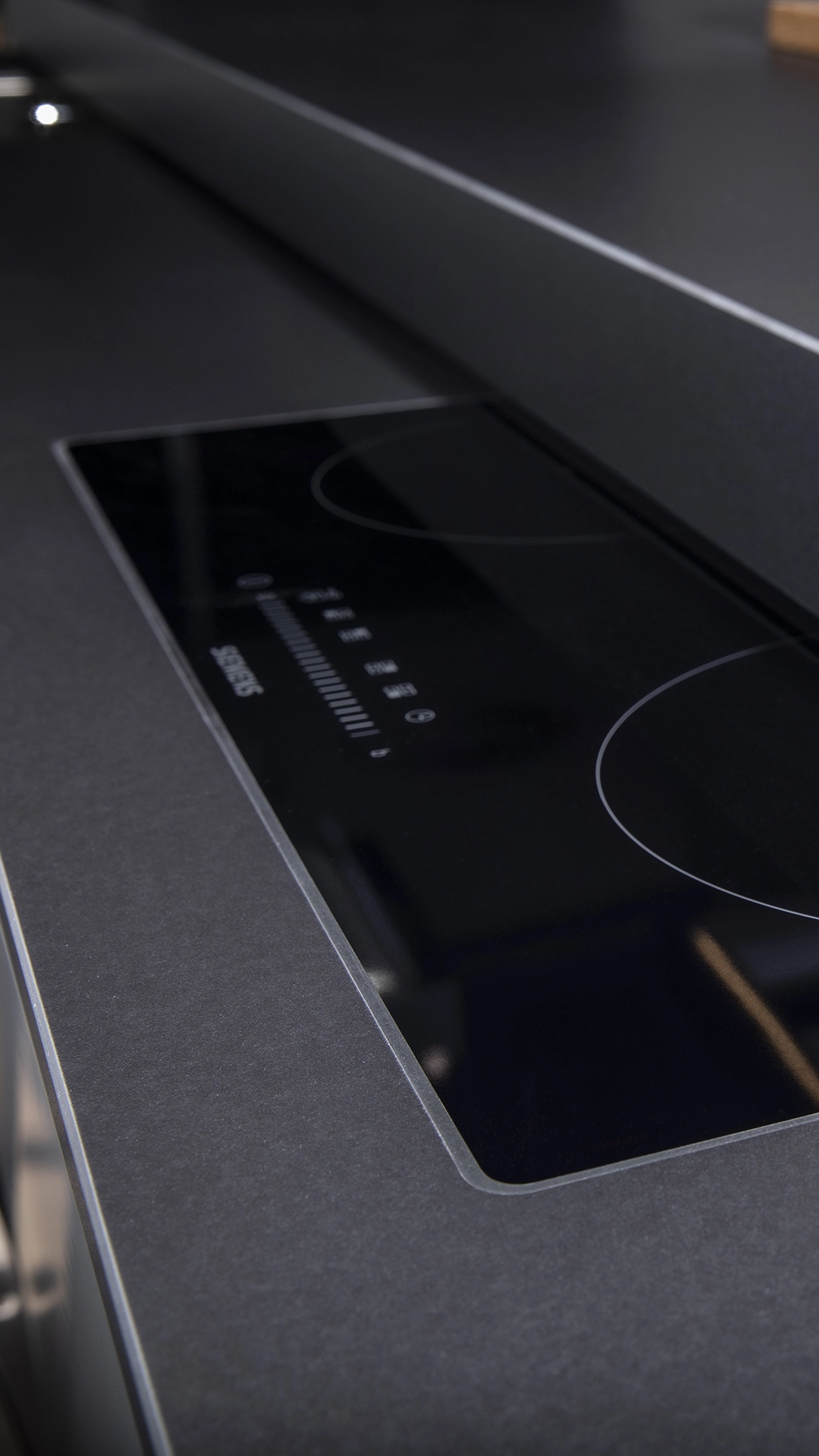 Close-up of a sleek black Siemens induction cooktop embedded in a dark kitchen countertop.