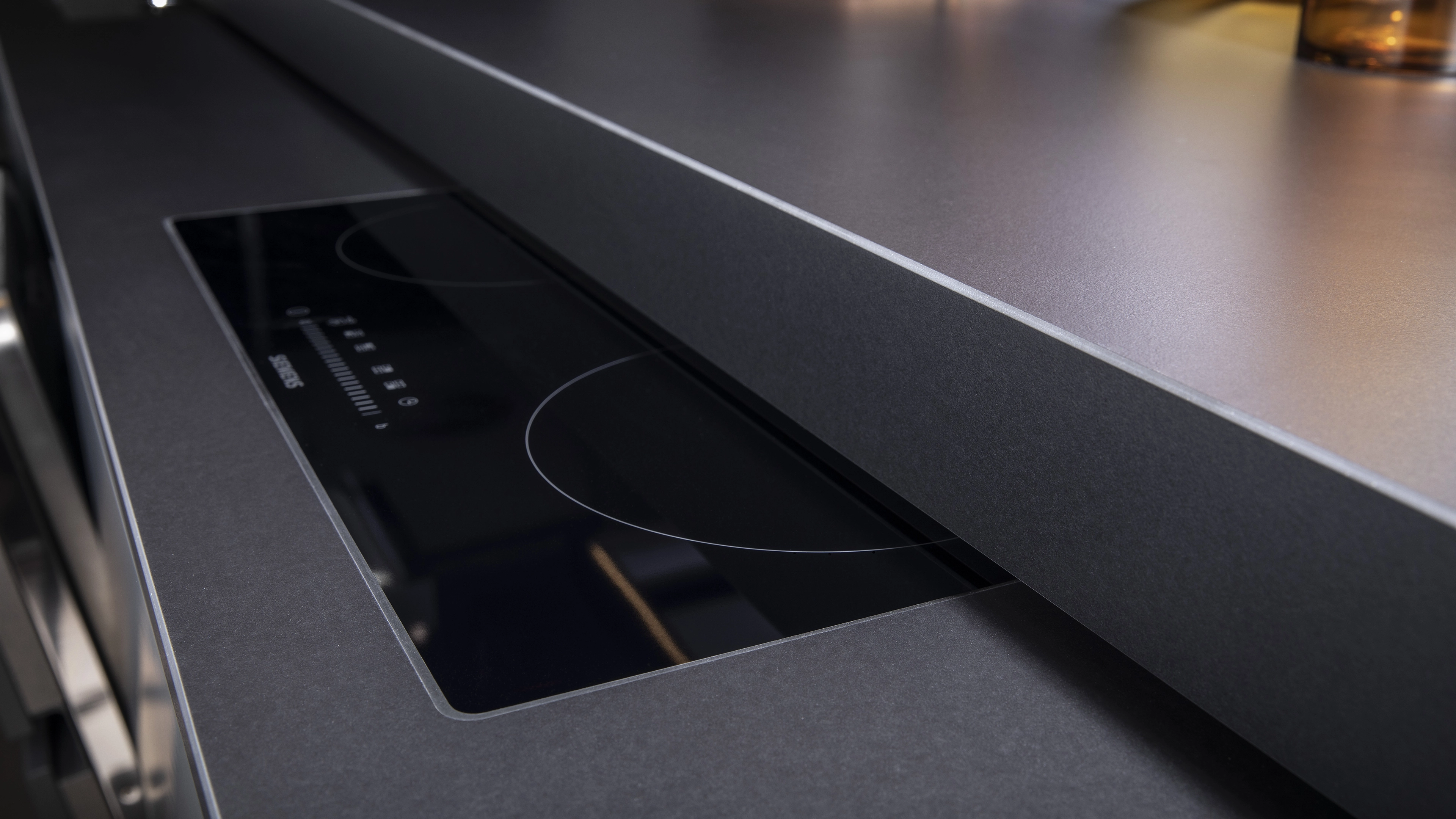 Close-up of a sleek black Siemens induction cooktop integrated into a dark kitchen countertop.