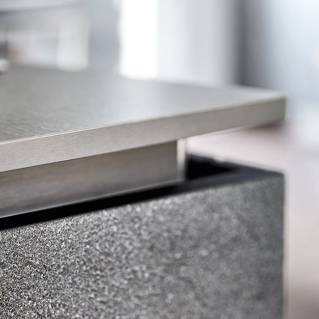 Close-up of a modern kitchen countertop edge with a smooth metallic surface above a textured dark stone drawer front.