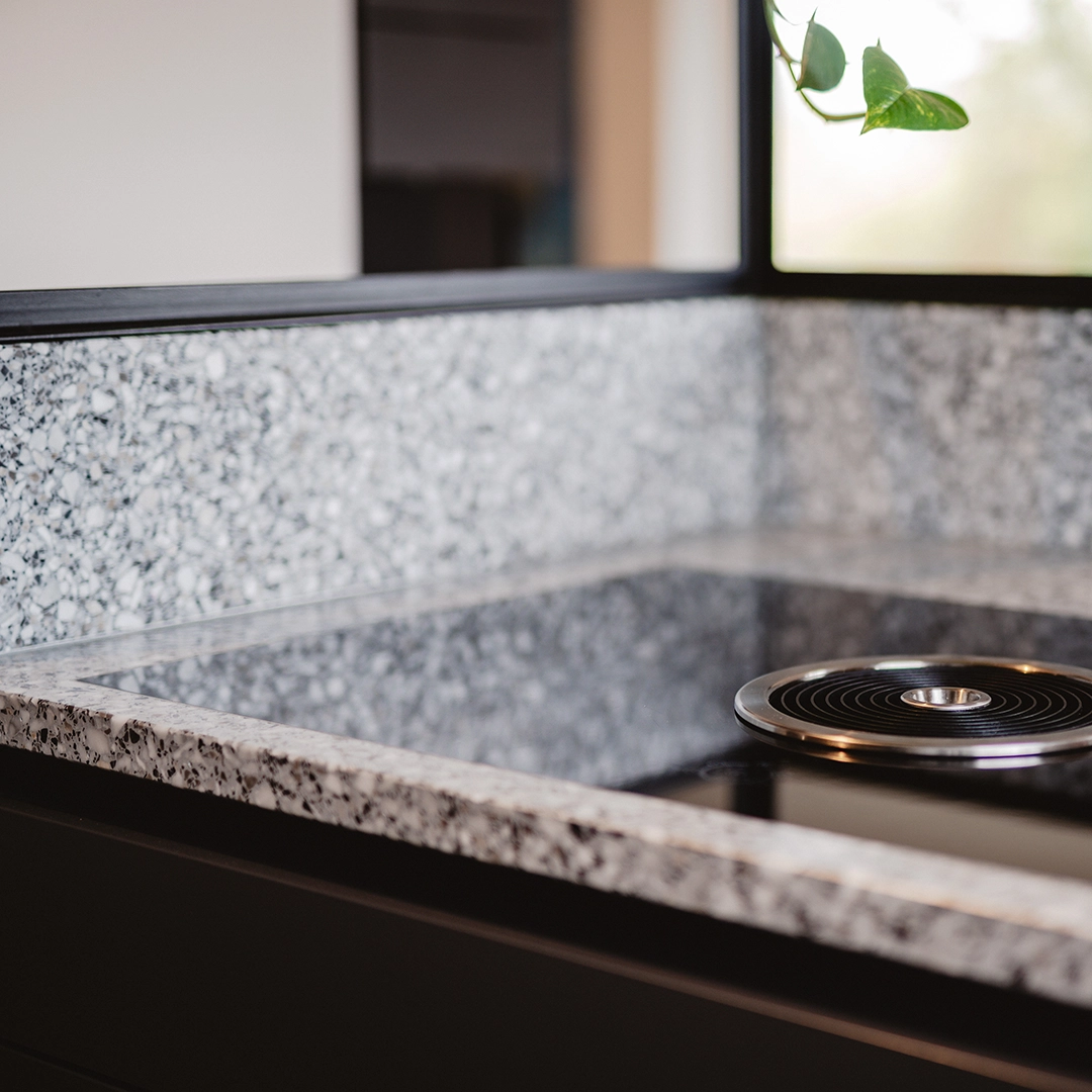 Close-up of a kitchen countertop with gray speckled surface and a black stovetop burner on the right side.