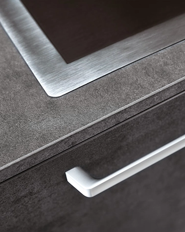 Close-up of a modern kitchen countertop with a brushed metal edge and a sleek white handle on a cabinet drawer.