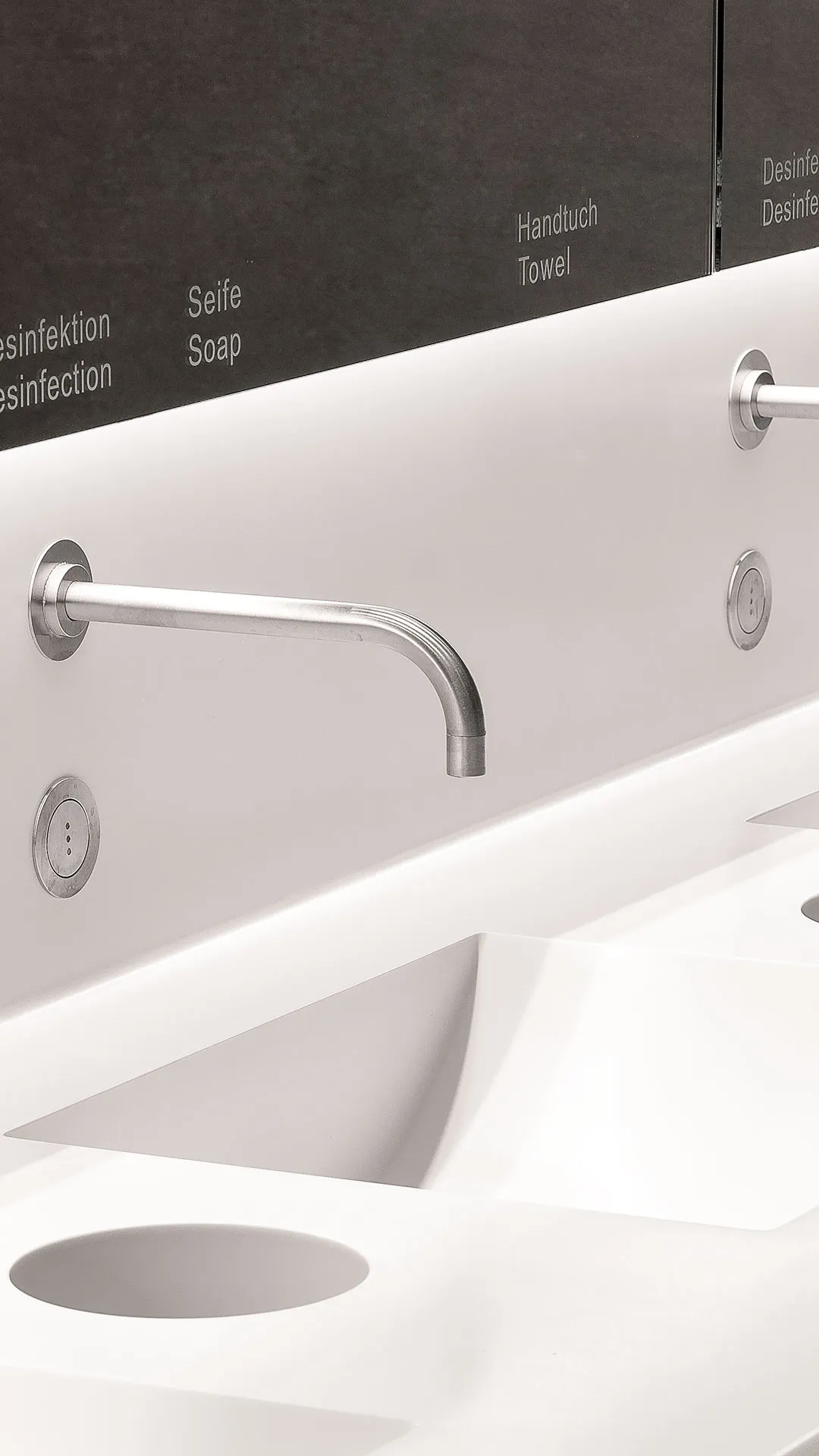 Modern white sink with wall-mounted stainless steel faucet and labeled dark cabinets above reading Soap, Towel, and Disinfection.