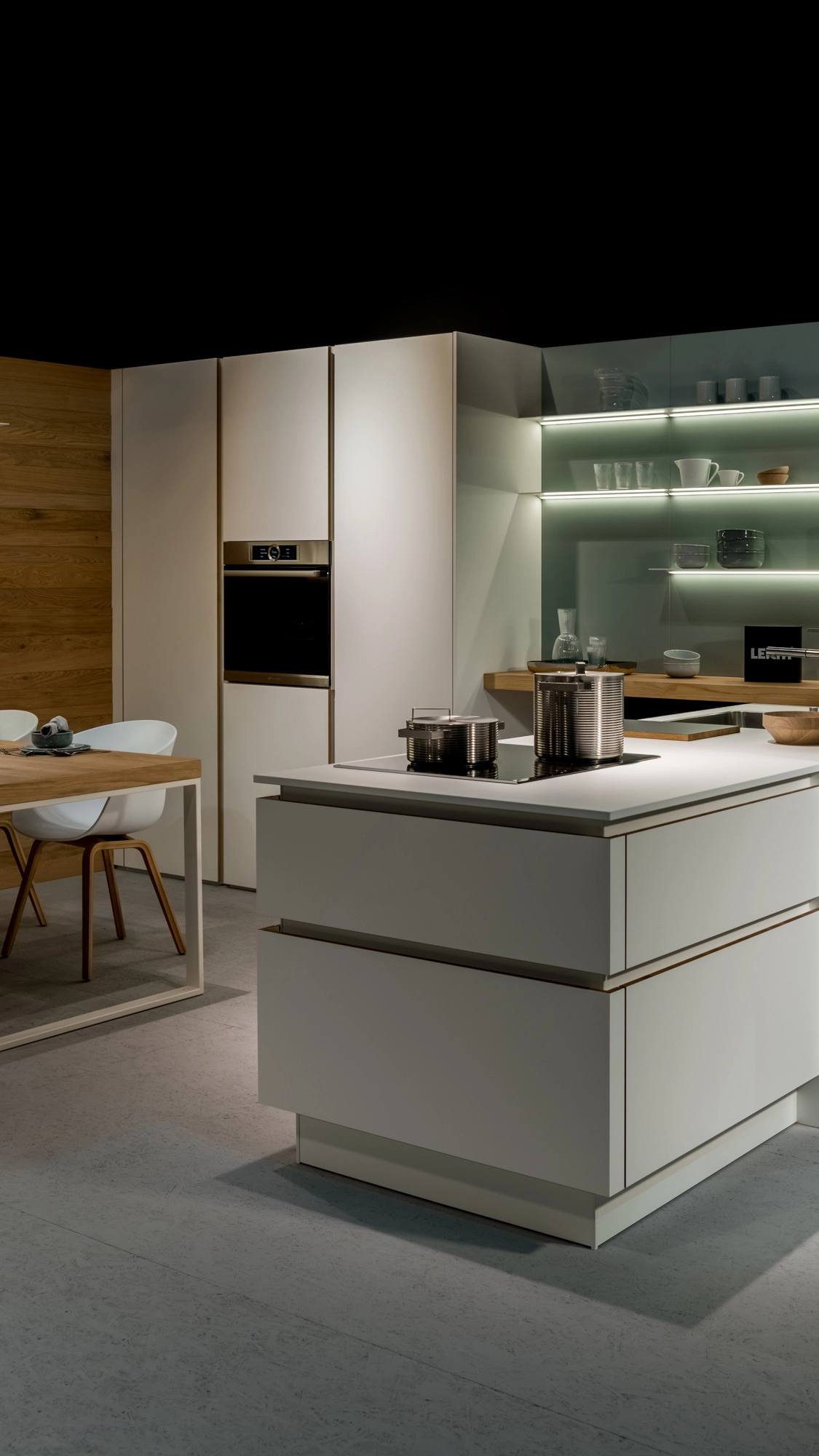 Modern kitchen with white cabinetry, built-in oven, kitchen island with induction cooktop and stainless steel pots, and a wooden dining table with white chairs.