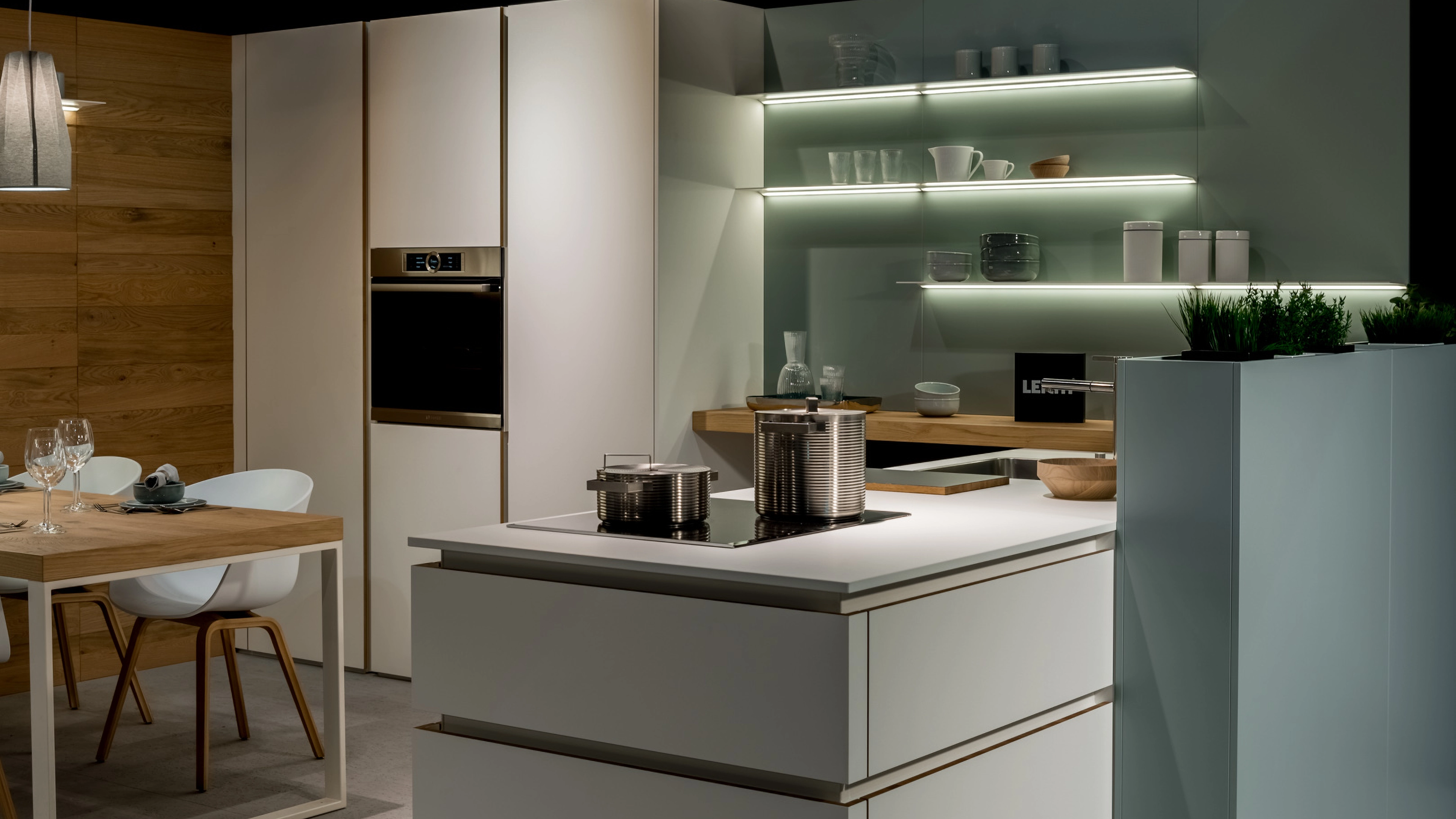 Modern kitchen with white cabinets, wooden dining table with white chairs, stove with pots, and built-in oven.