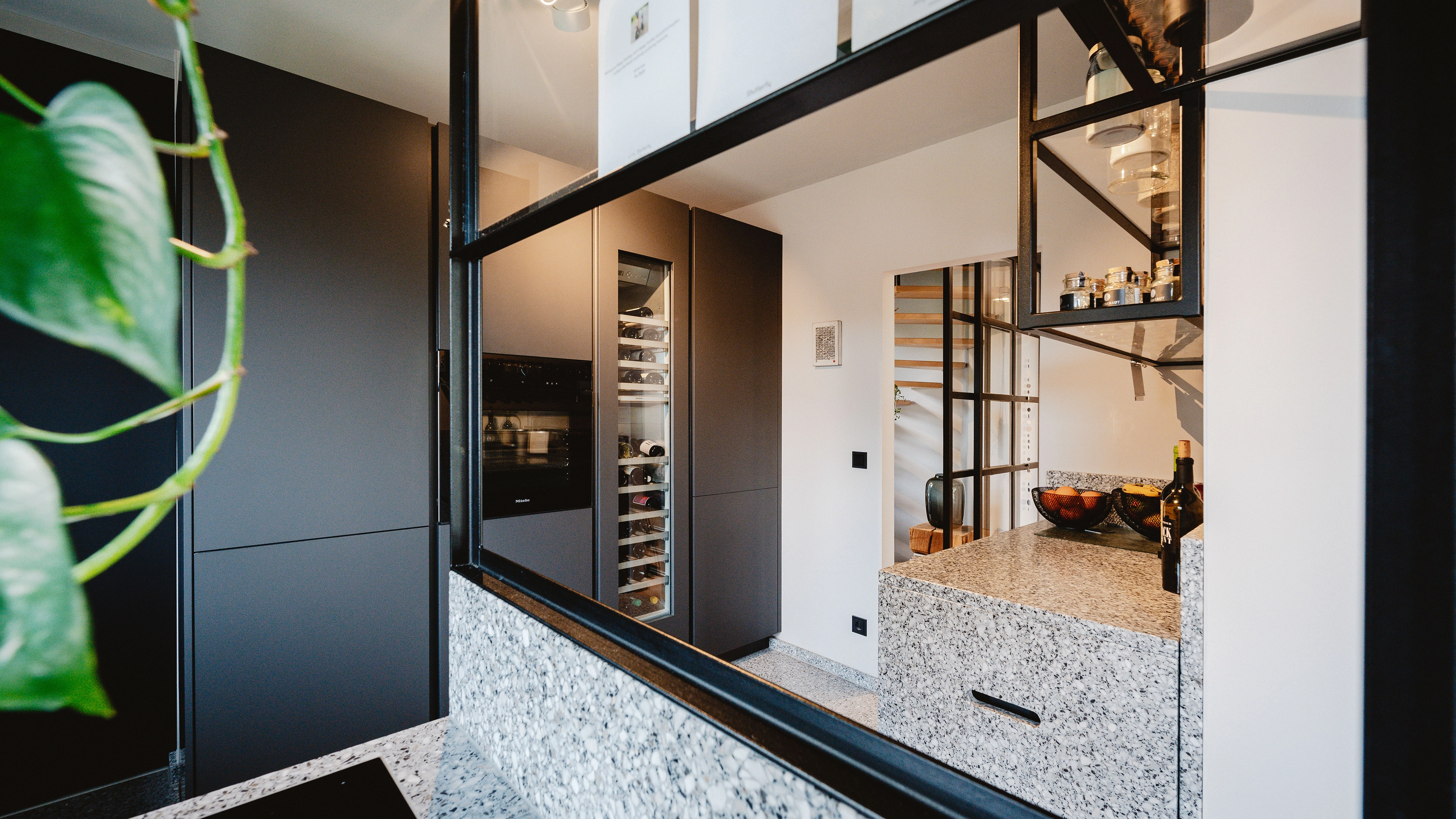 Modern kitchen with black cabinetry, built-in wine cooler, granite countertops, and black-framed glass partition.