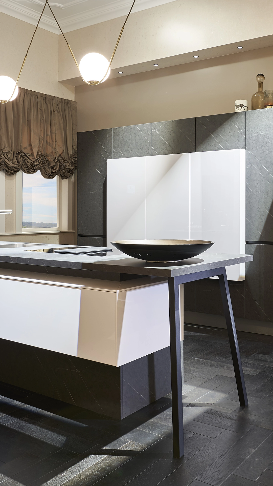 Modern kitchen with a large marble island, white cabinets, dark stone wall panels, and two round pendant lights.