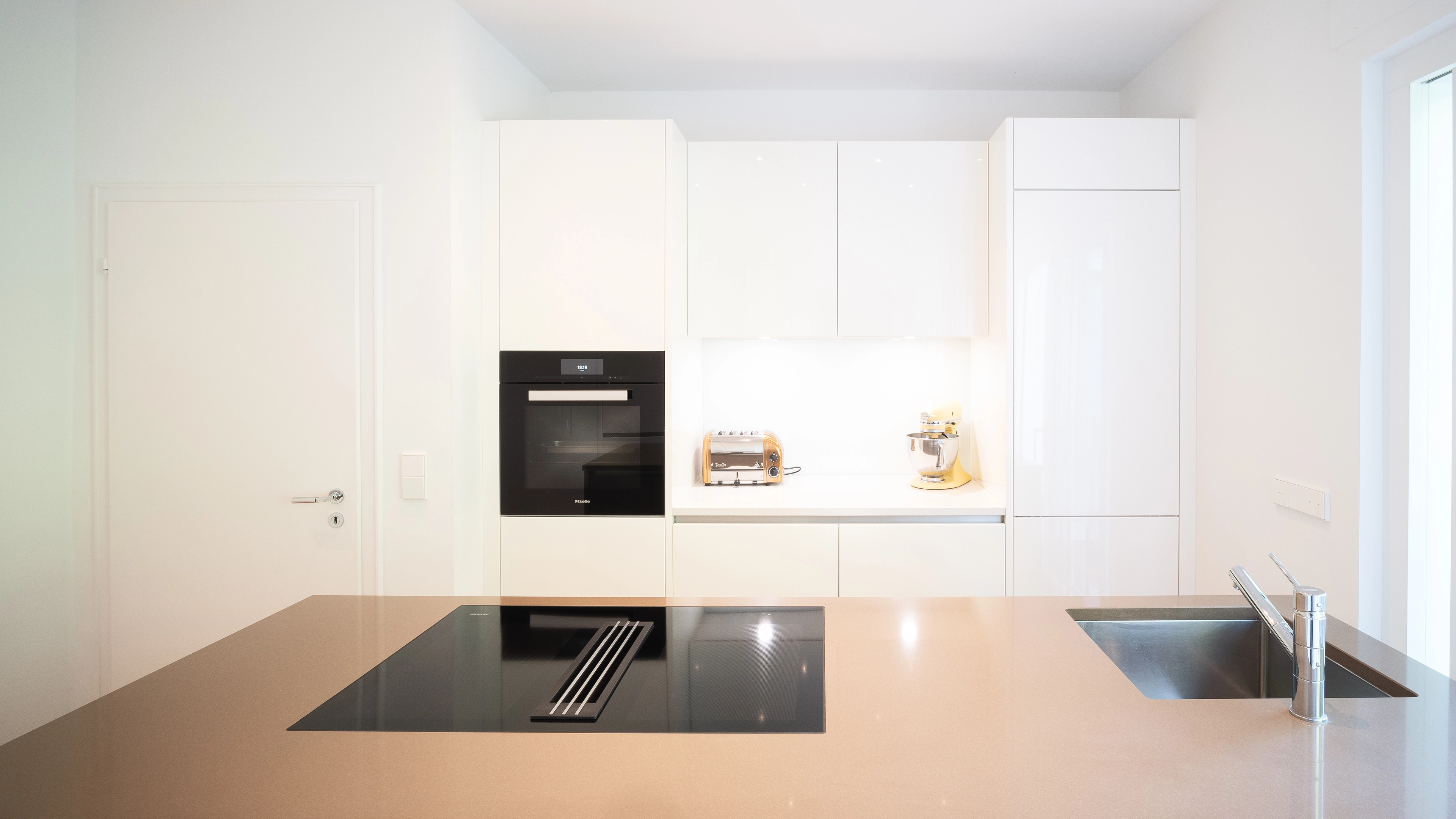 Modern white kitchen with built-in oven, toaster, stand mixer, induction cooktop, and sink.