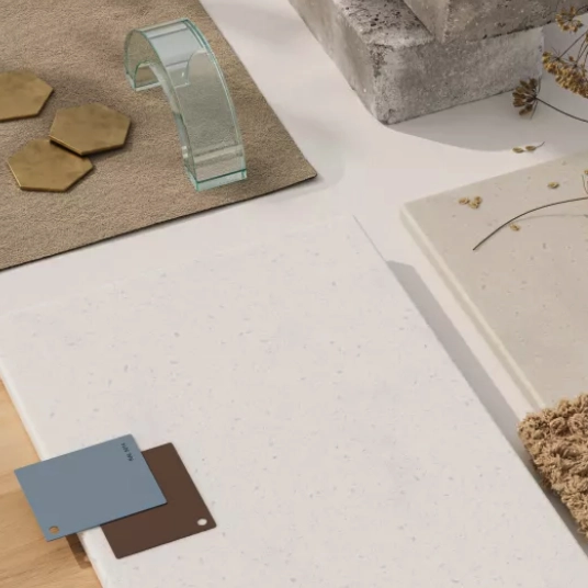 White speckled solid surface countertop sample with material swatches, hexagonal tiles, glass decor, and textured fabric on top.
