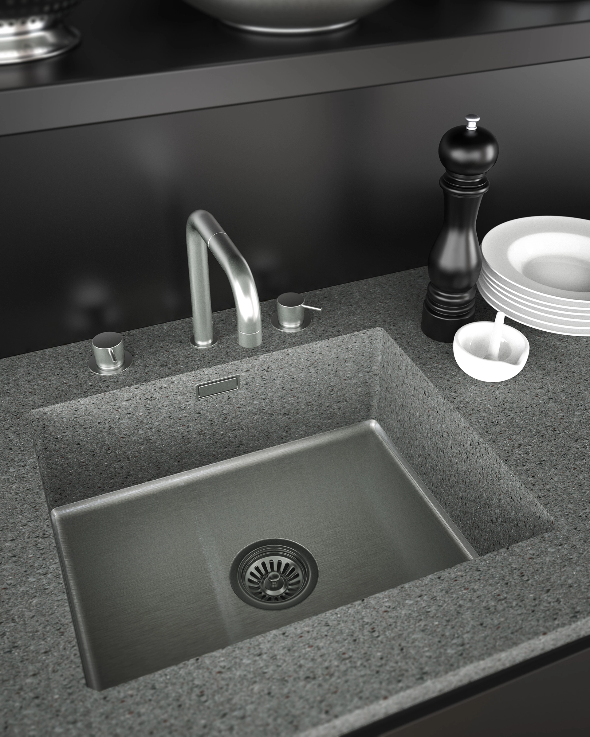 Modern kitchen sink with brushed metal faucet set in a speckled gray countertop, next to a black pepper grinder and stacked white plates.