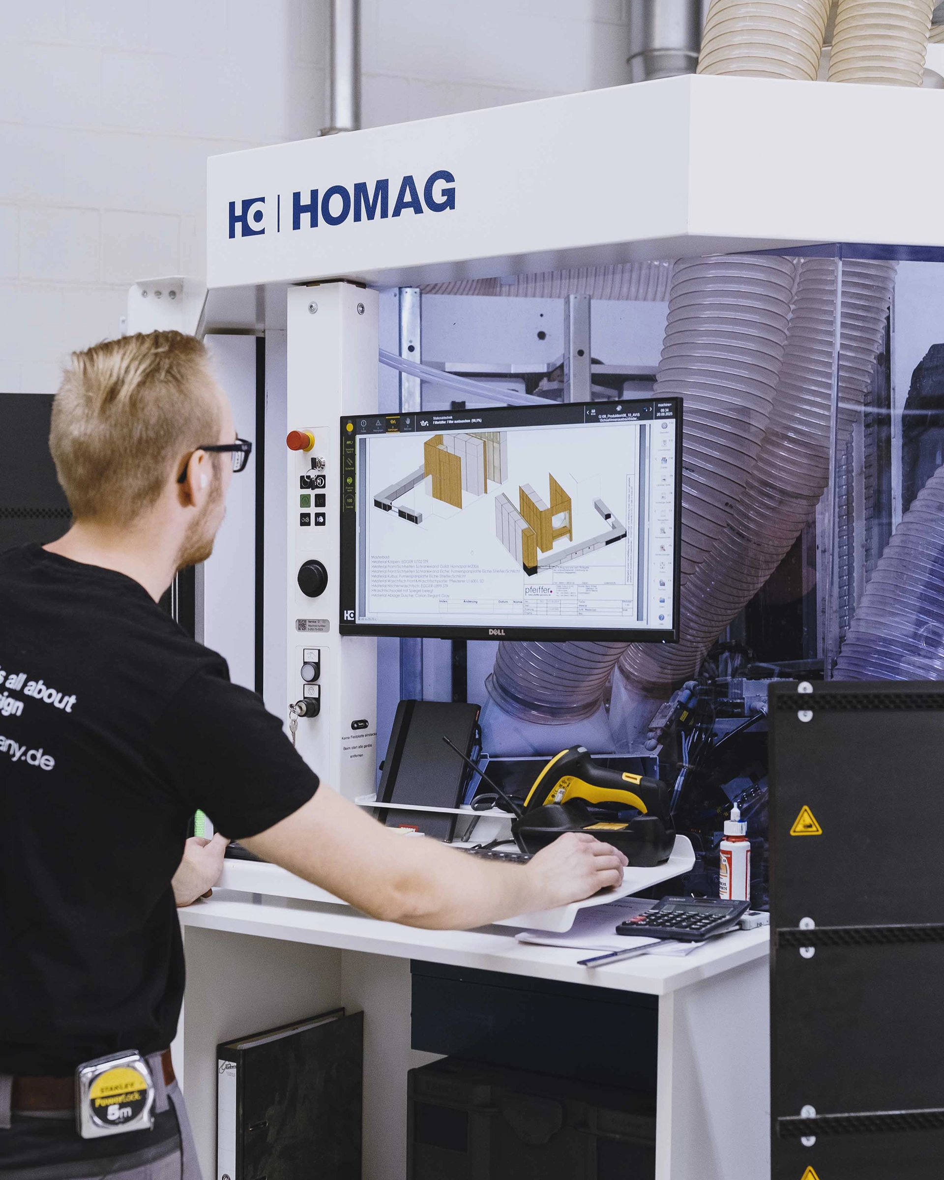 Man operating a HOMAG machine, viewing 3D wood panel design on a computer screen in an industrial setting.