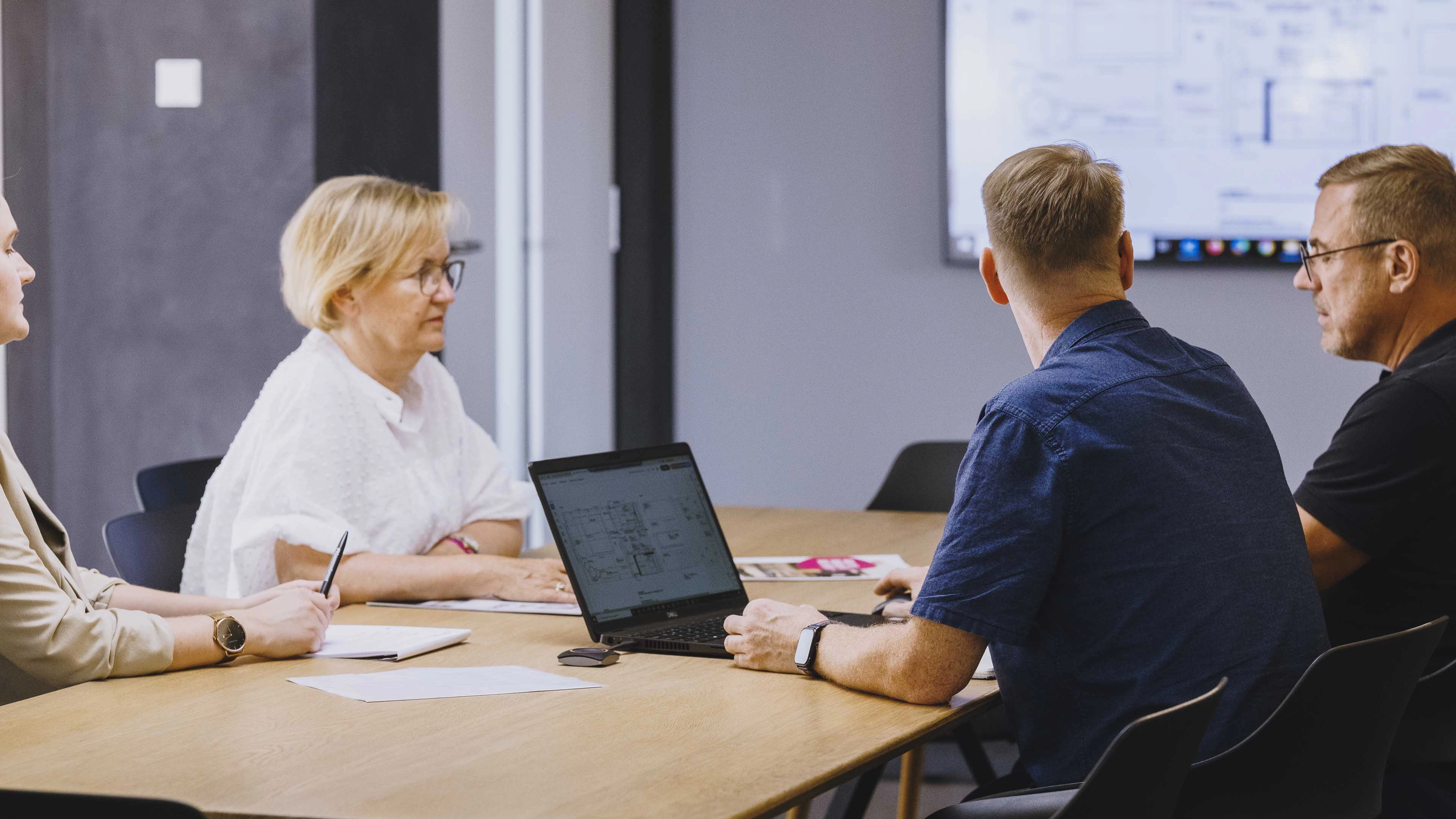 Four professionals seated around a conference table during a meeting, with a laptop and documents in front of them.