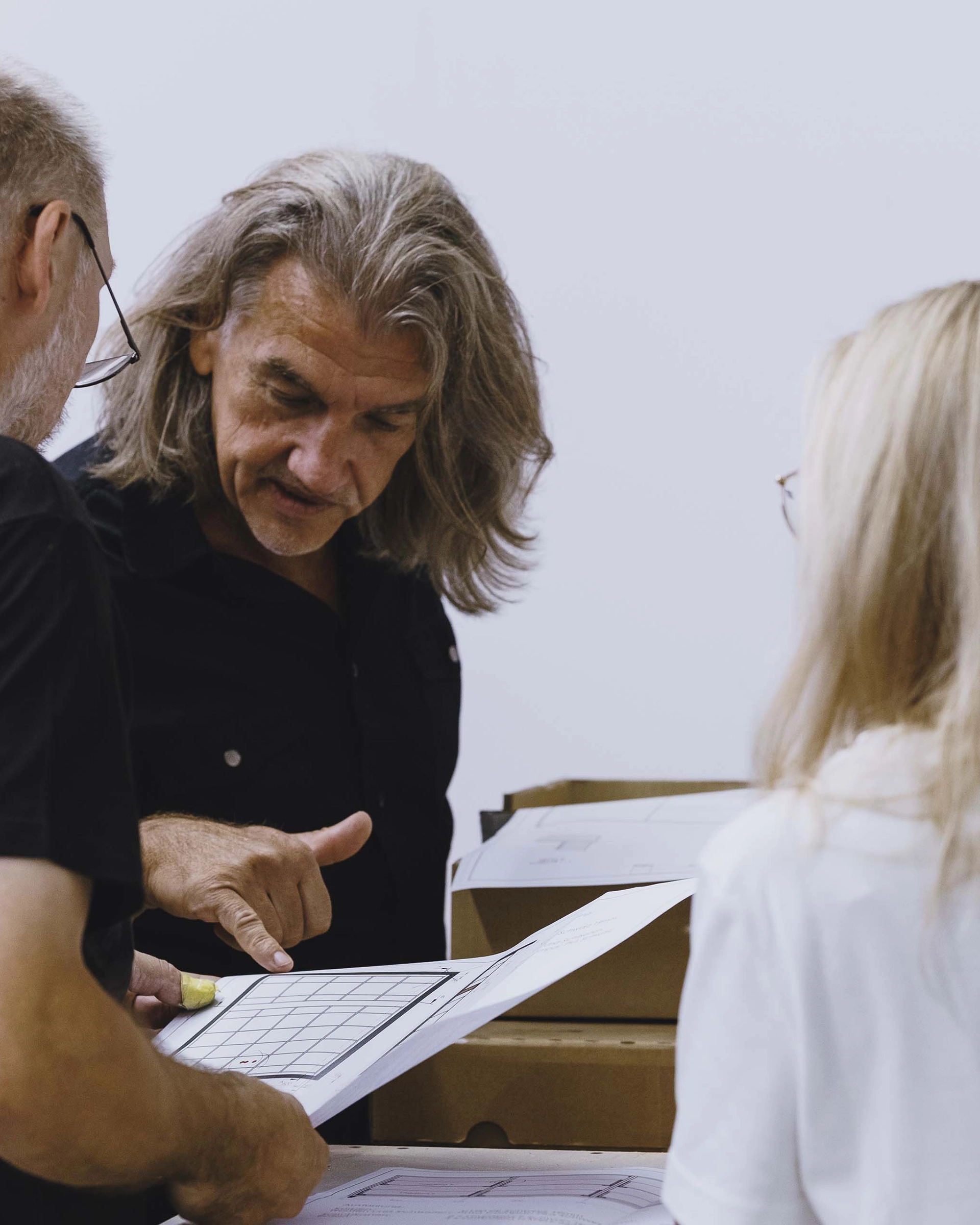 Three people examining architectural plans together, with one man pointing at a blueprint.