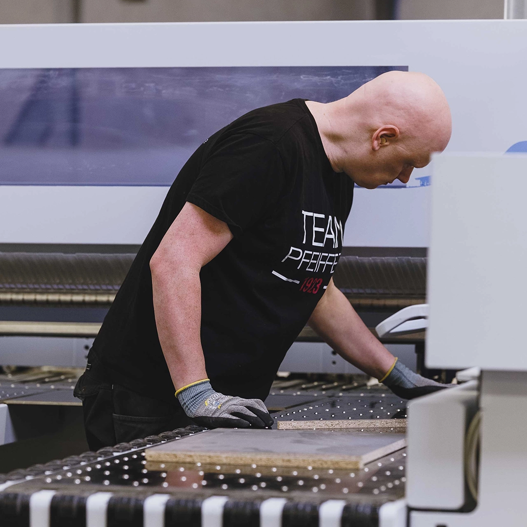 Worker wearing gloves inspecting a piece of wood on a machine in a factory.