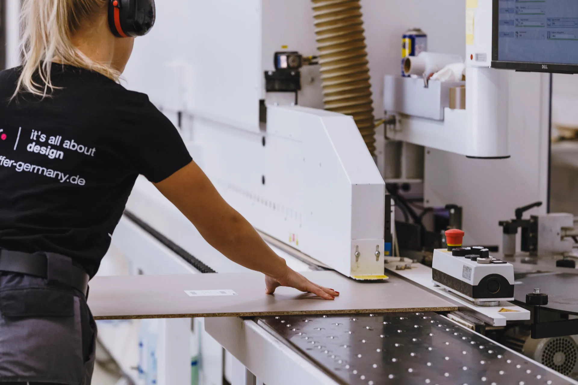 Person wearing ear protection operating a machine to process a sheet of wood or similar material.