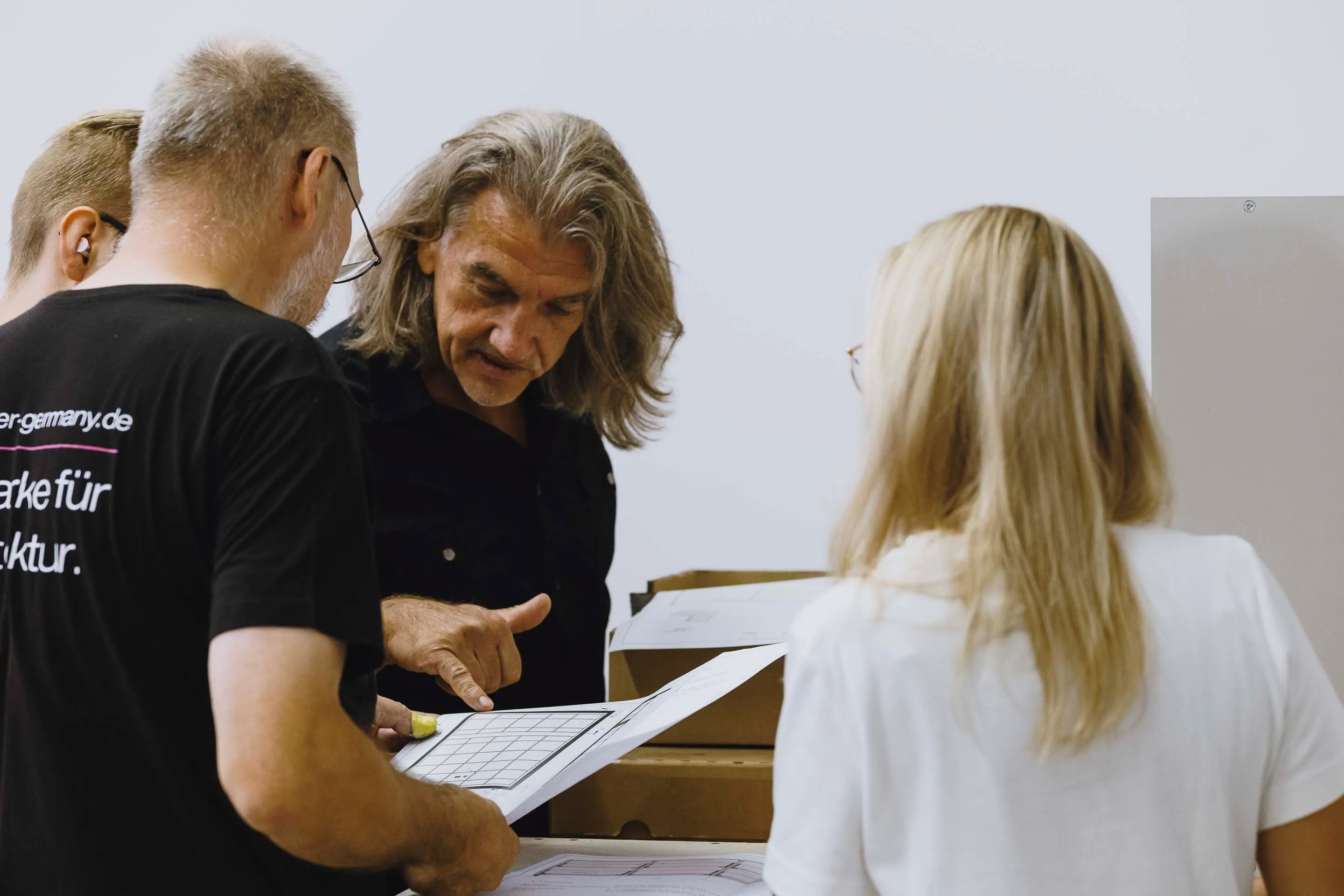 Four people standing close together reviewing architectural plans or blueprints.
