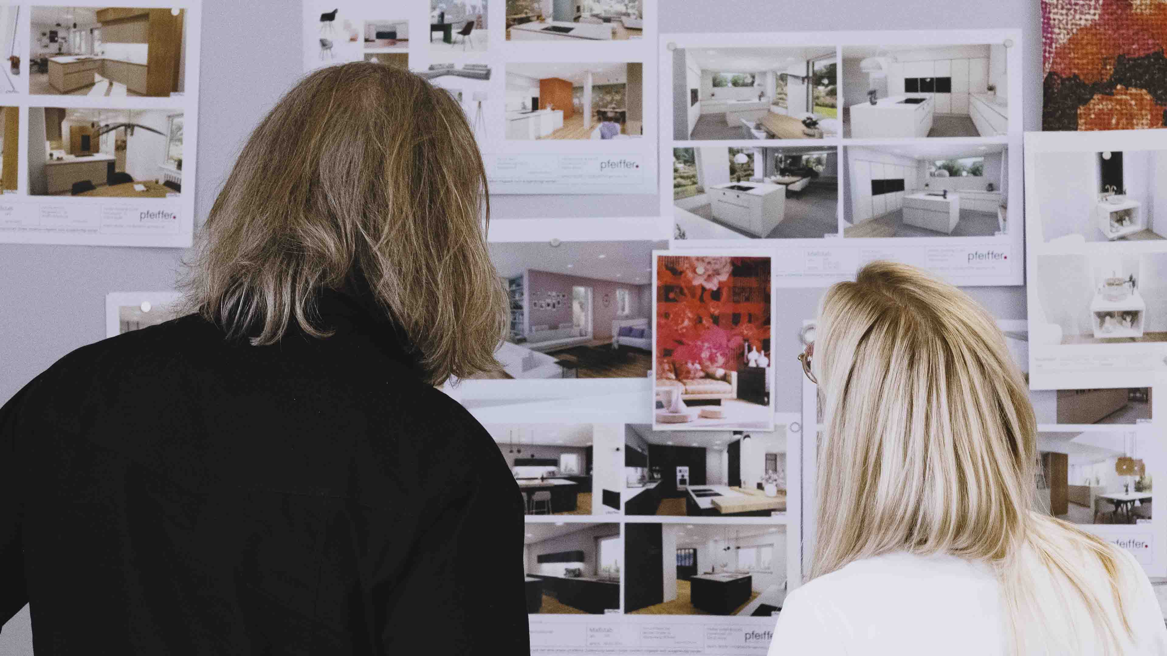Two people viewing a wall covered with pinned architectural and interior design photos.