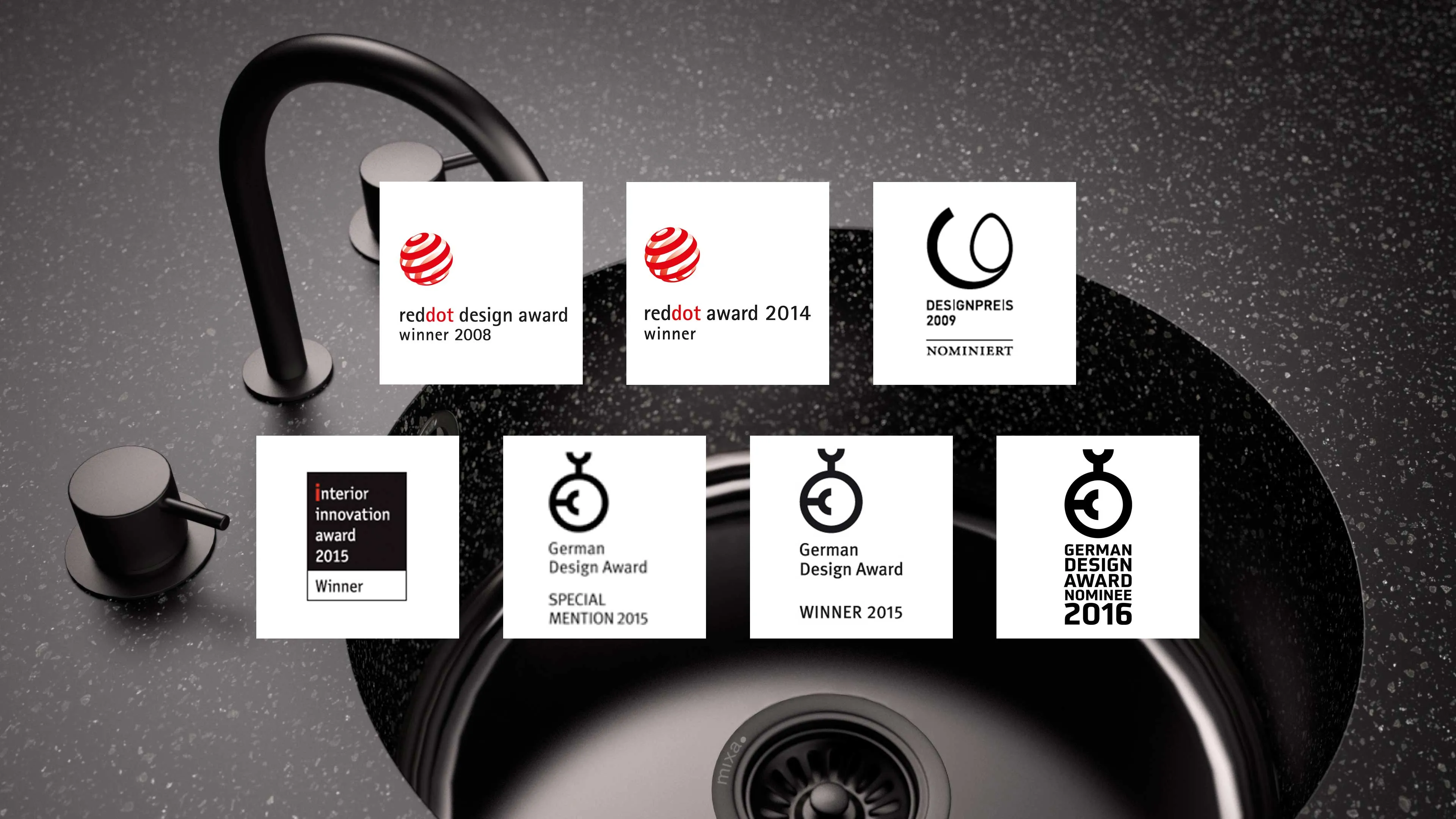 Black kitchen sink with matte black faucet on speckled countertop featuring logos of various design awards including Red Dot 2008 and 2014 winners, Designpreis 2009 nominee, Interior Innovation Award 2015 winner, and German Design Awards from 2015 and 2016.