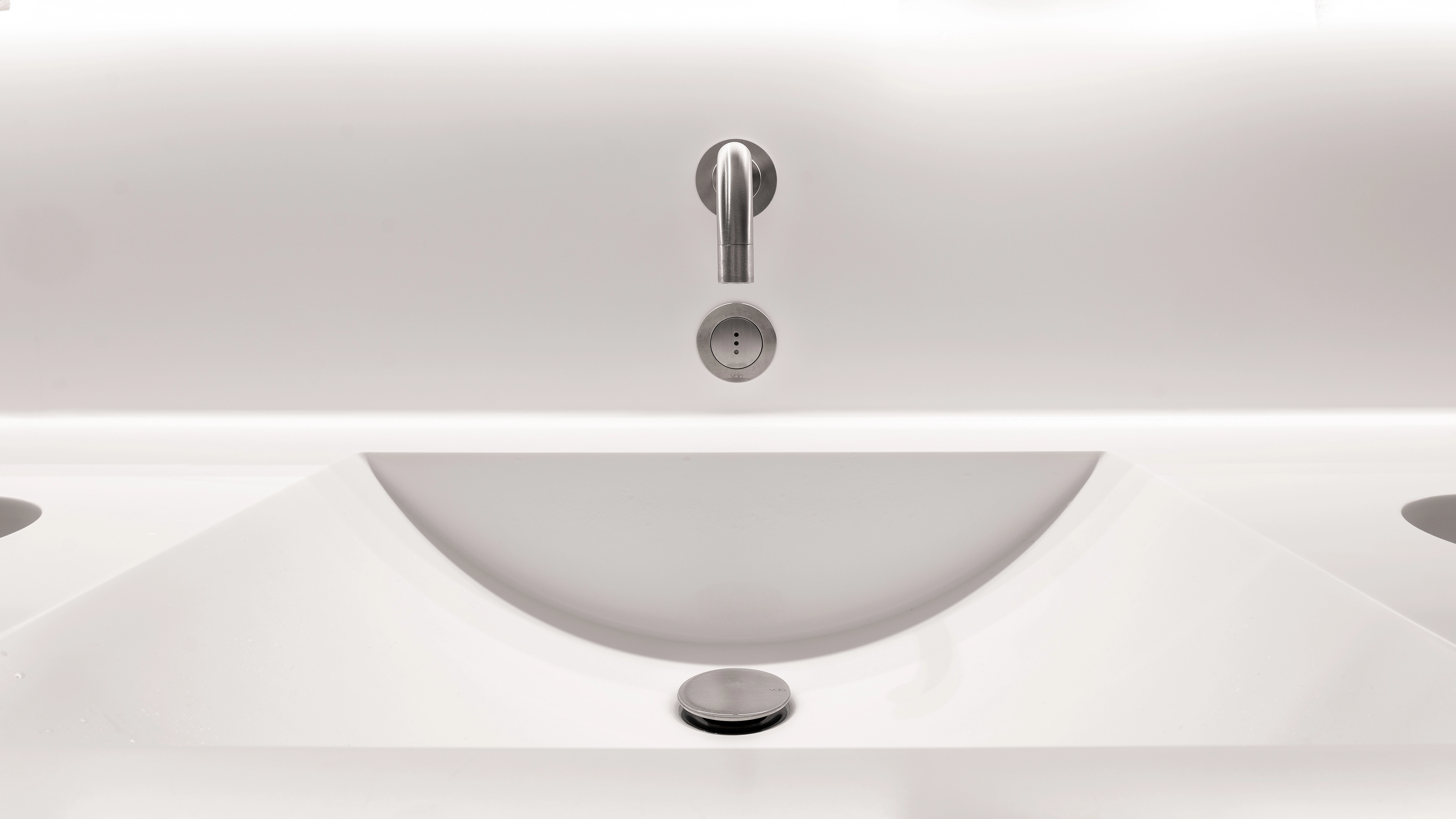 Minimalist white bathroom sink with a modern stainless steel faucet and drain stopper.