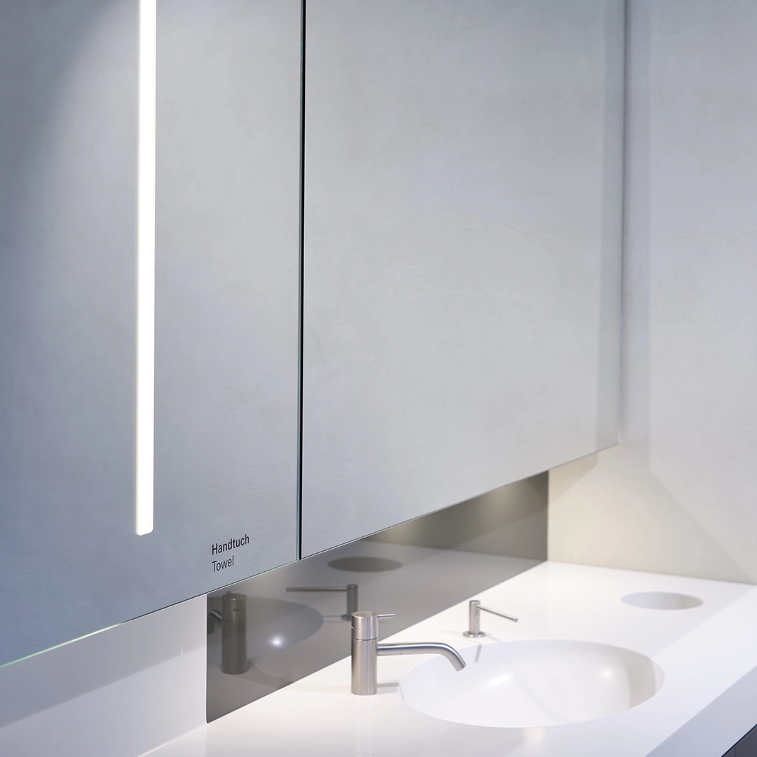 Modern bathroom sink with a round basin, a sleek faucet, and a glossy mirrored cabinet above labeled 'Handtuch Towel'.