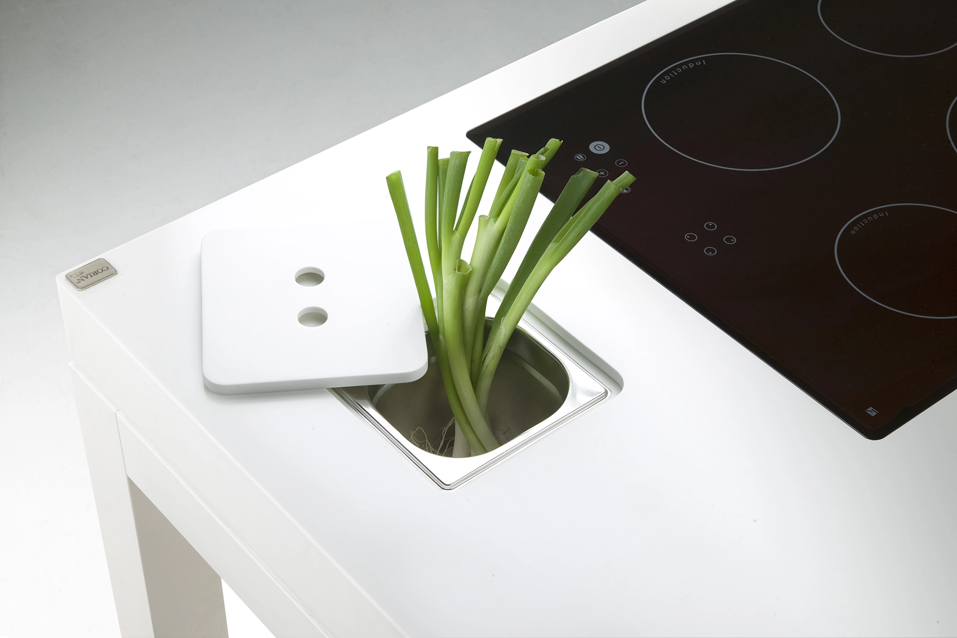White kitchen countertop with black induction stove and green onions growing in a built-in planter.