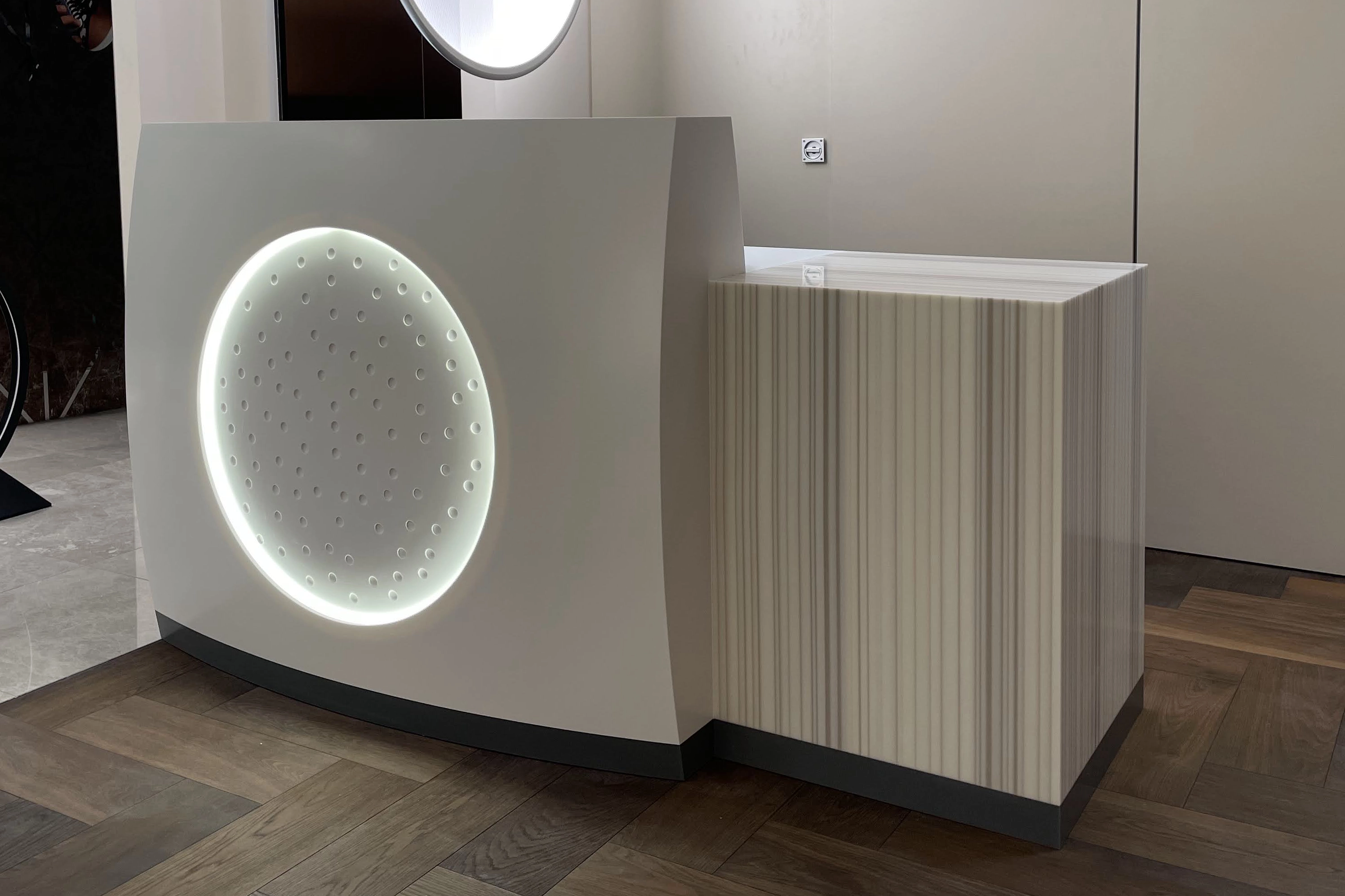 Modern kitchen island with a circular illuminated panel featuring perforations and a striped wooden side panel on a parquet floor.