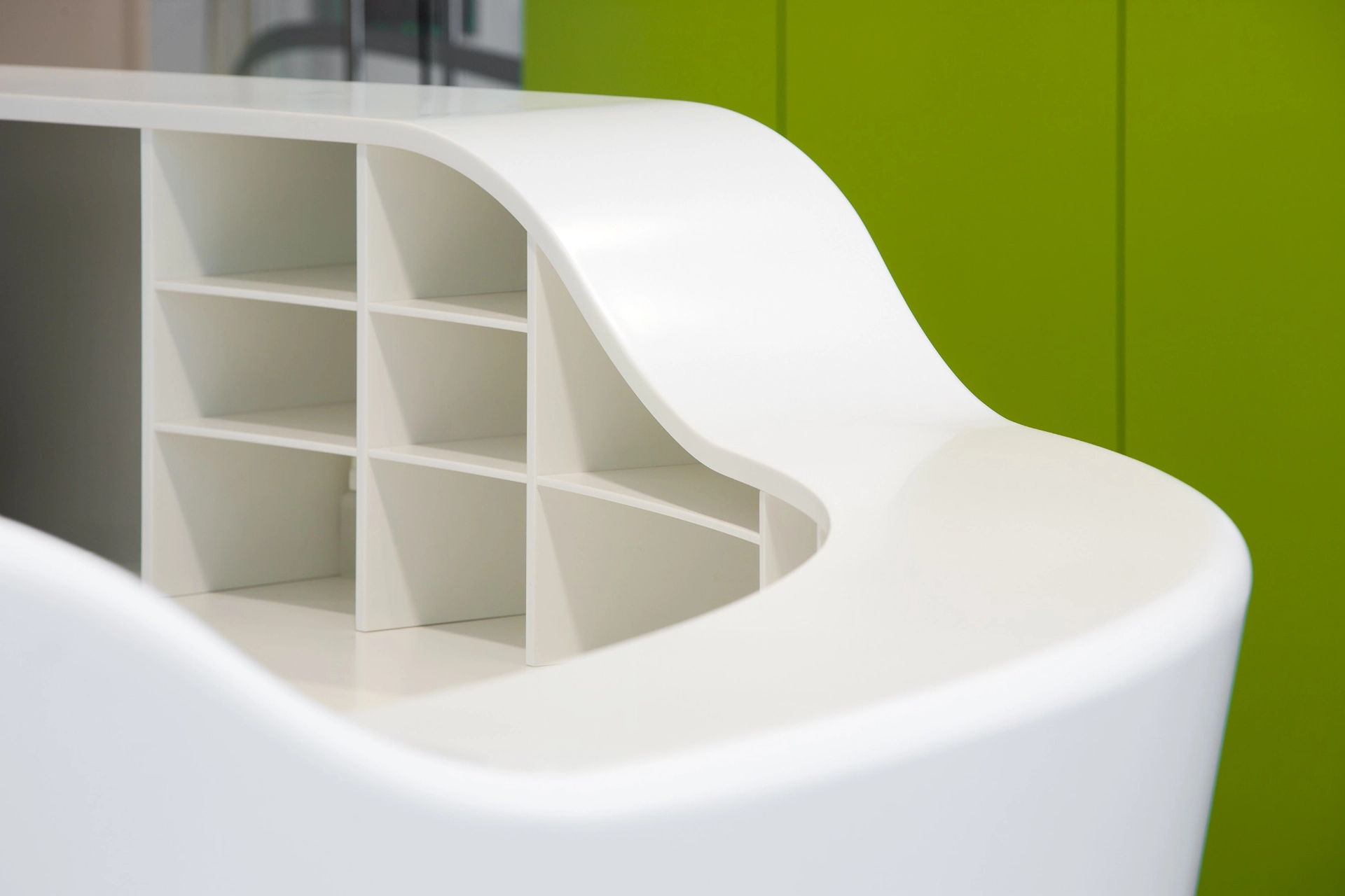 Curved white countertop with built-in shelves against a green wall.