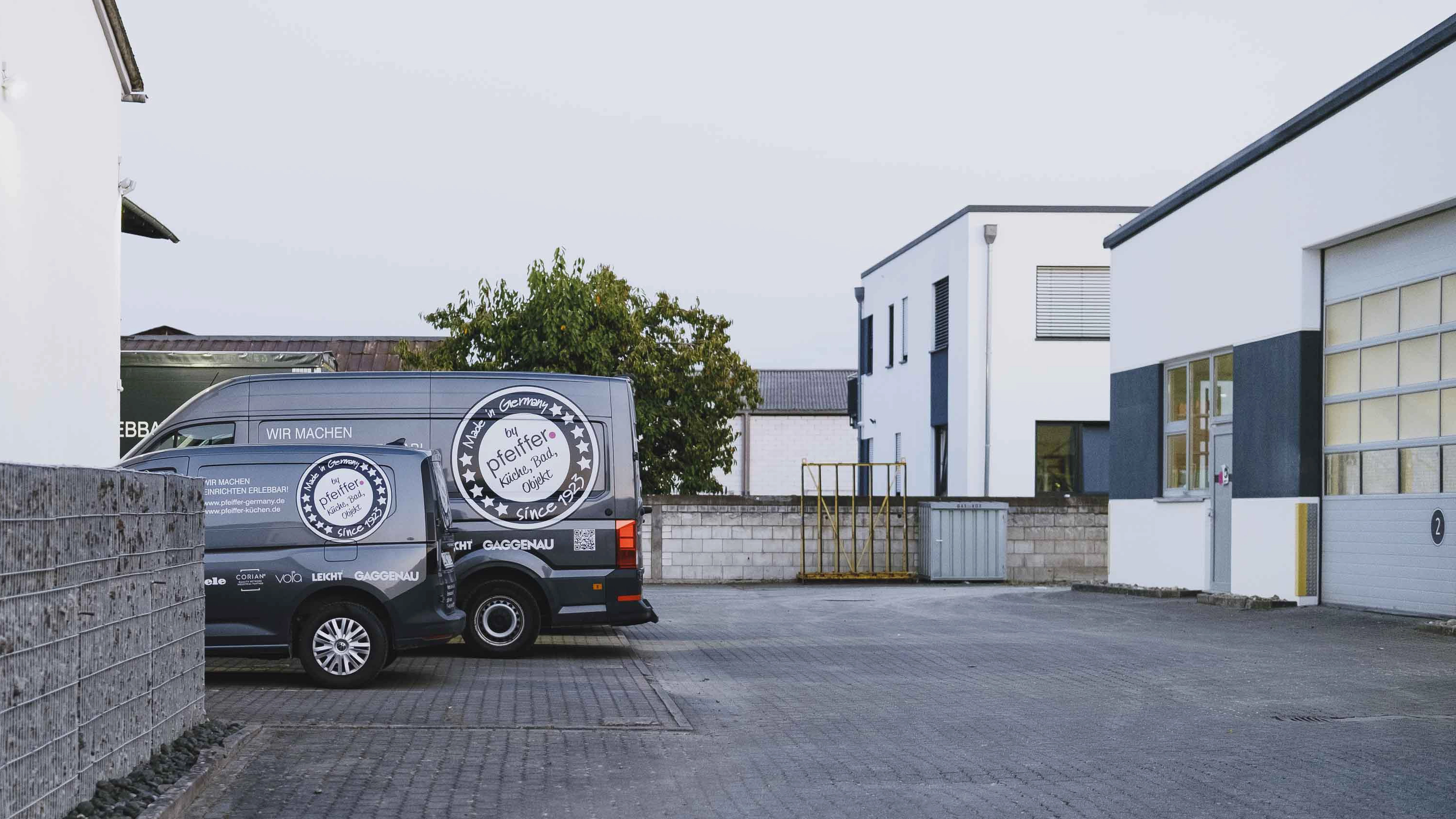 Two dark blue company vans parked in front of white and gray modern commercial buildings.