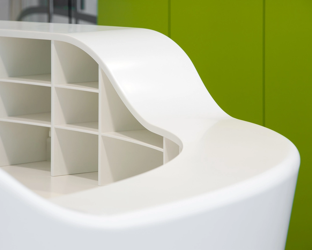 Curved white modular shelving unit with multiple compartments against a green wall.