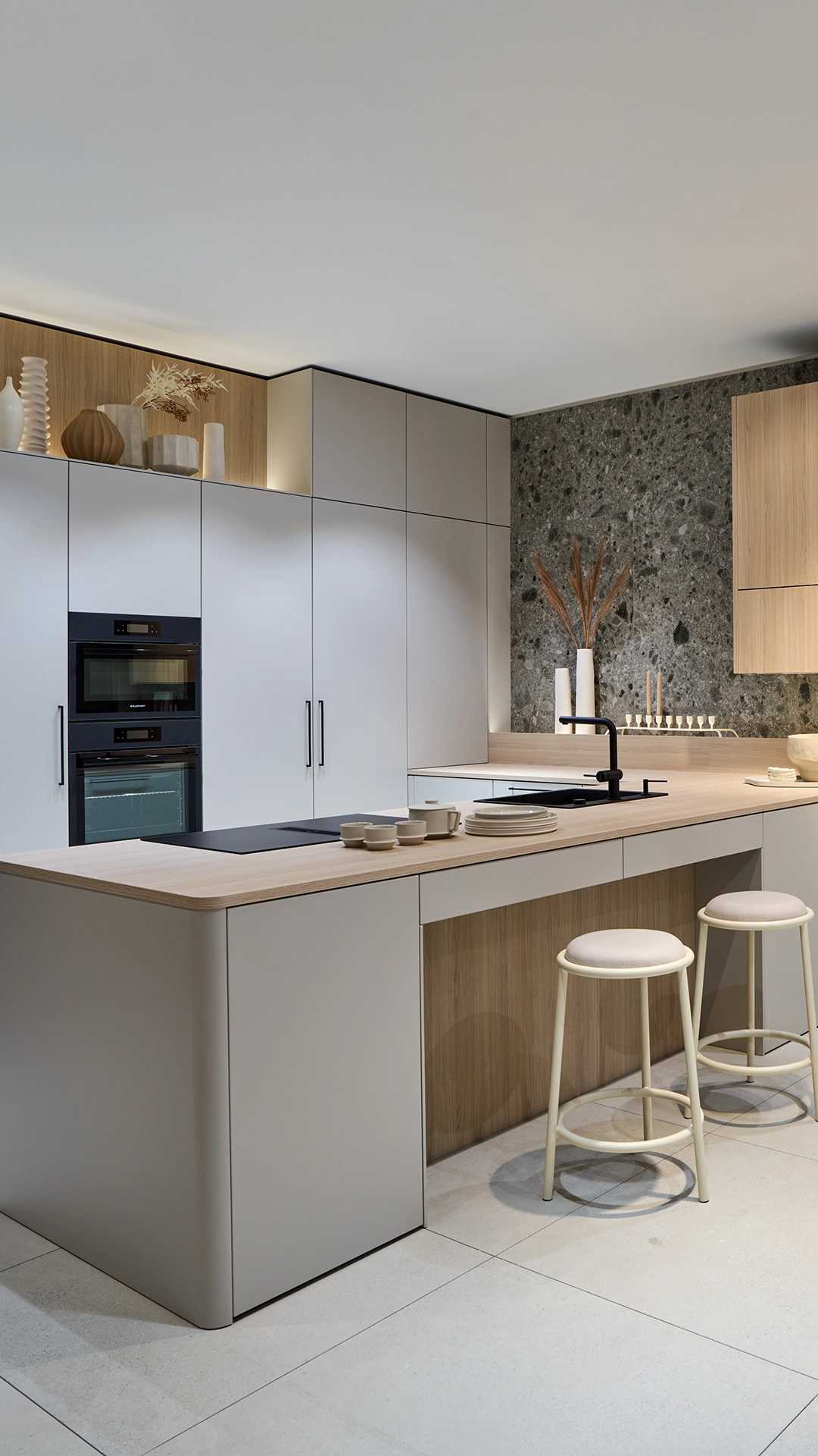 Moderne Küche mit Kücheninsel in beige und Holz, eingebautem Ofen, zwei Hockern und Dekoration auf der Arbeitsplatte.