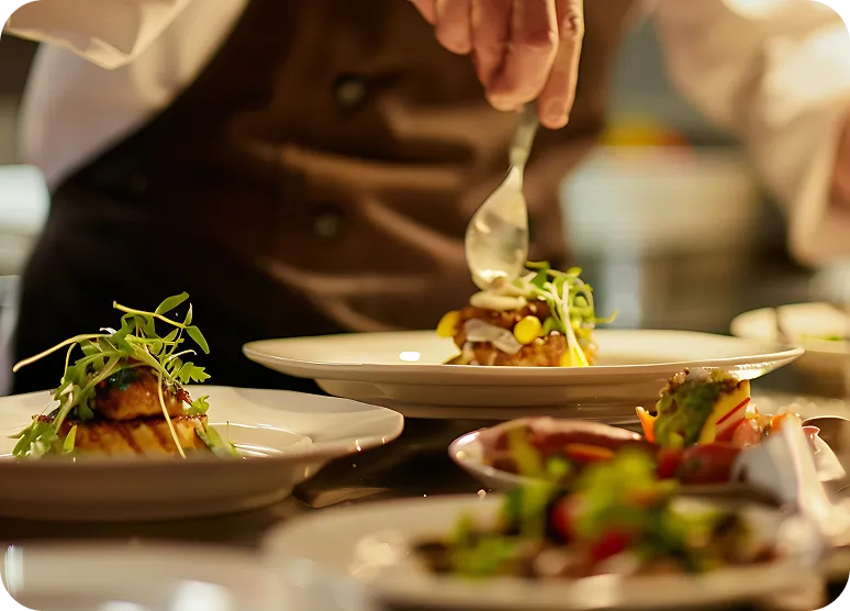Chef plating gourmet dishes topped with fresh greens in a professional kitchen.