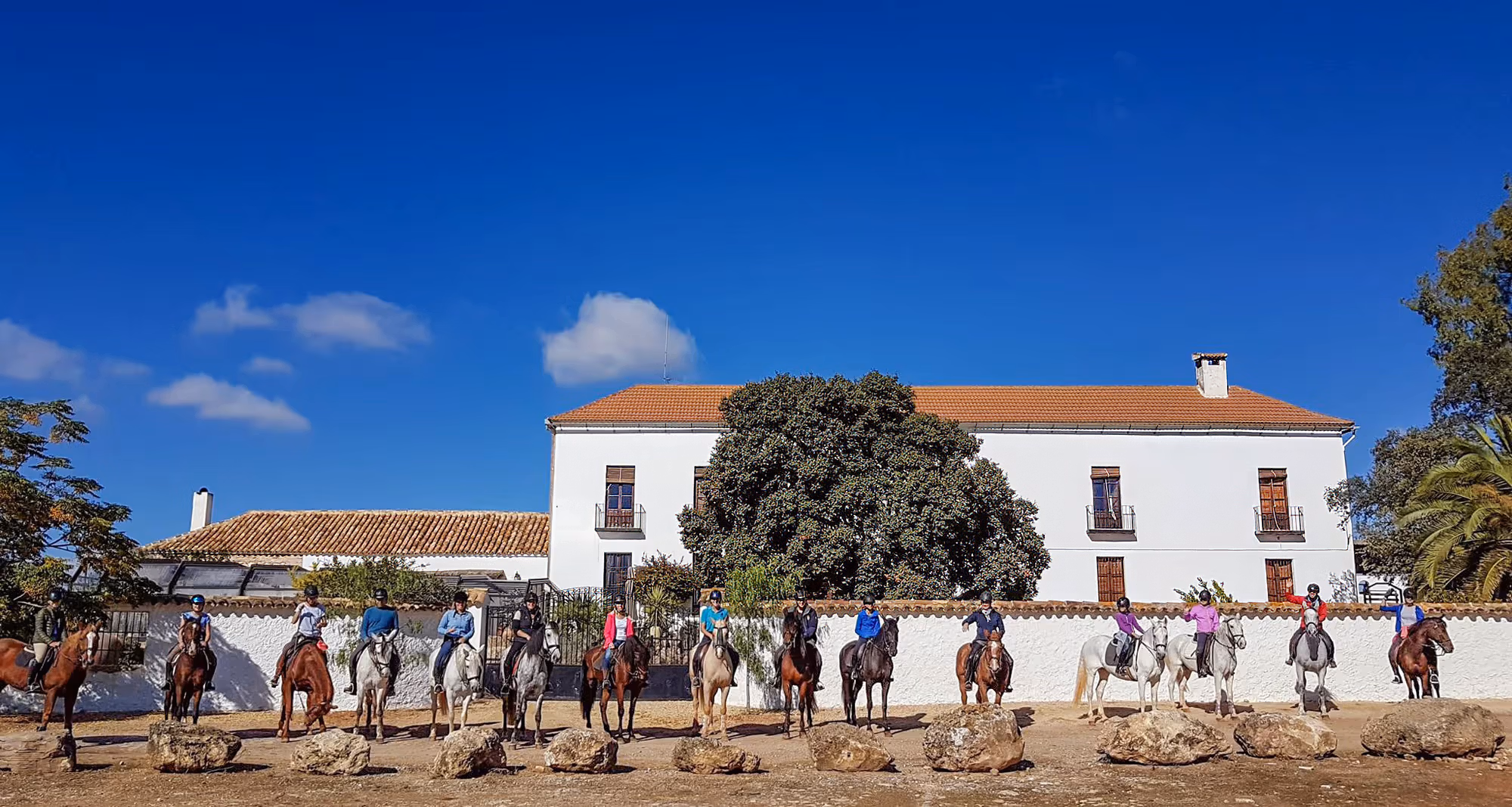 A group of horse riders posing for a photo in front of the hacienda at the beginning of an Andalusia horse riding holiday.