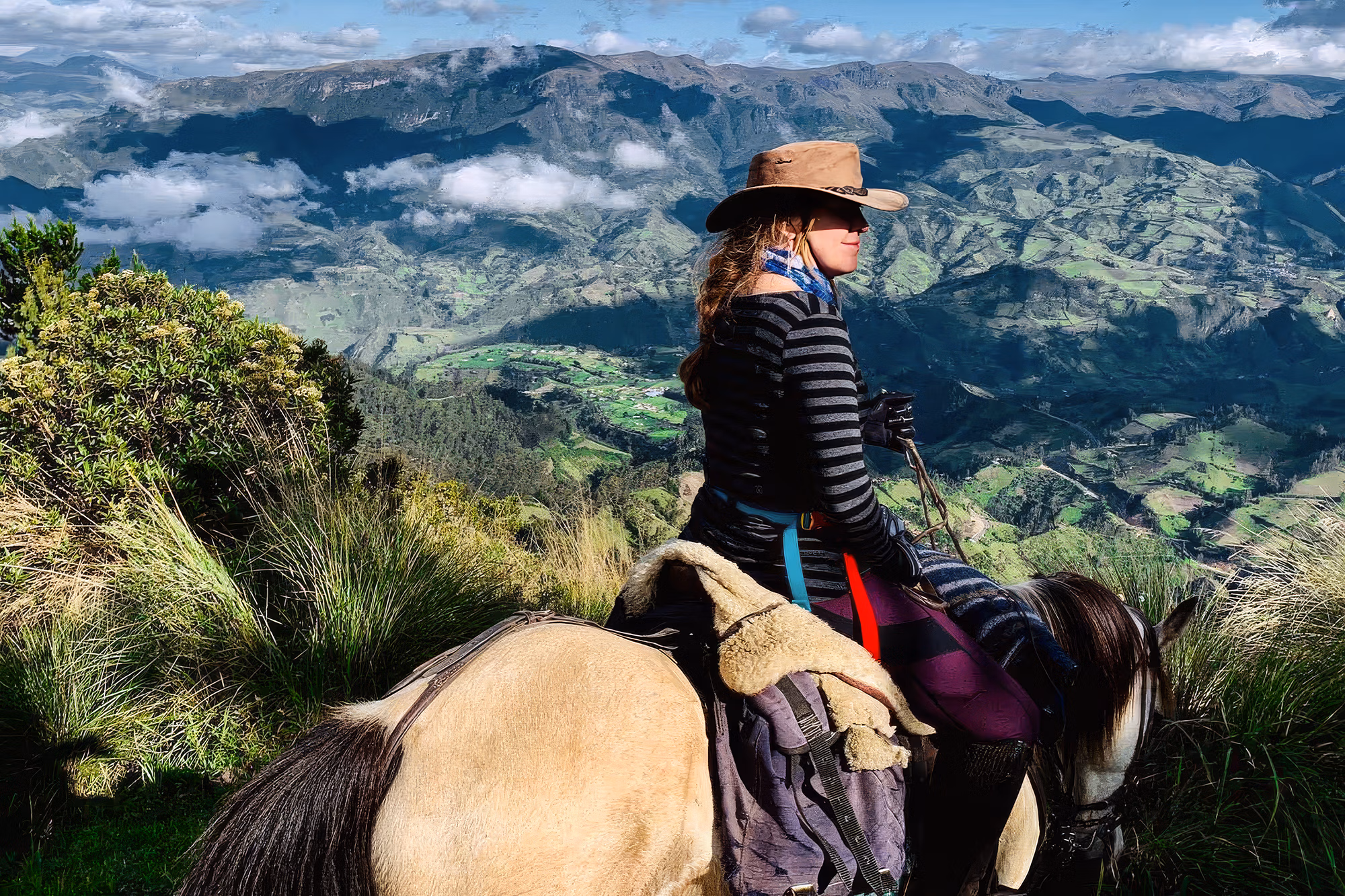 Side view of a woman on horseback wearing a sun hat with the stunning Andes mountains behind her during an Avenue of the Volcanoes horse trek.