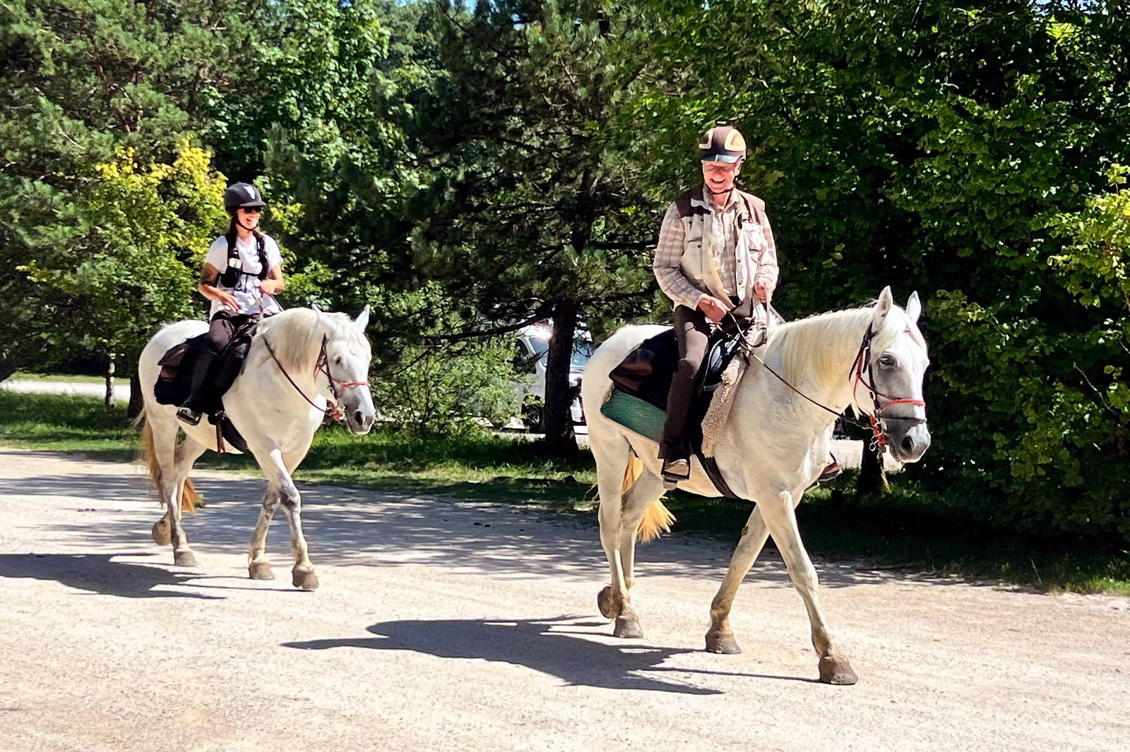 Two riders on white horses traveling along a lush green path