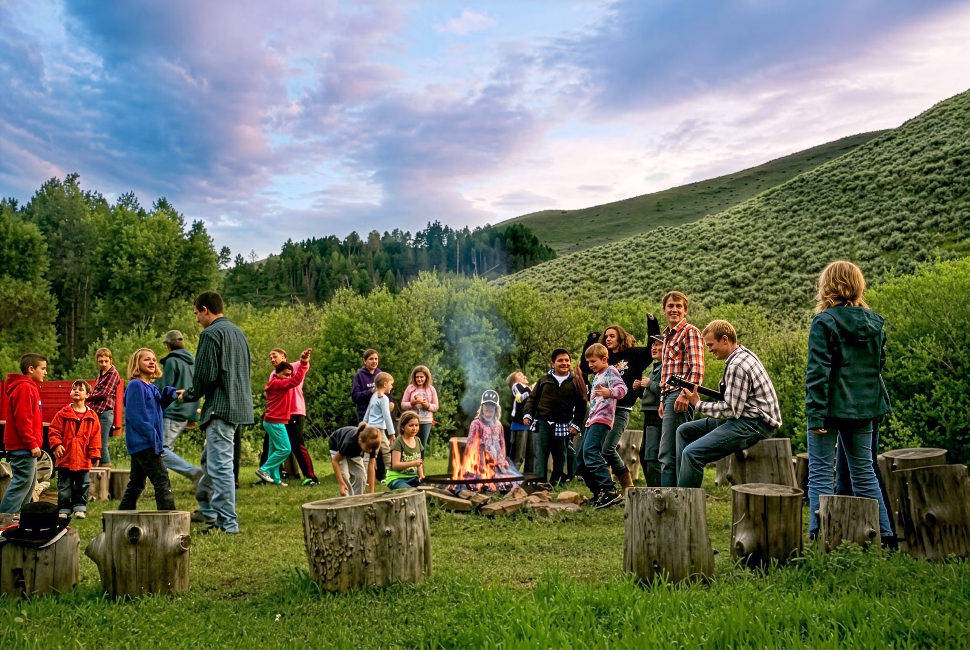 A group of horseback riders sitting around a cozy campfire right after sunset