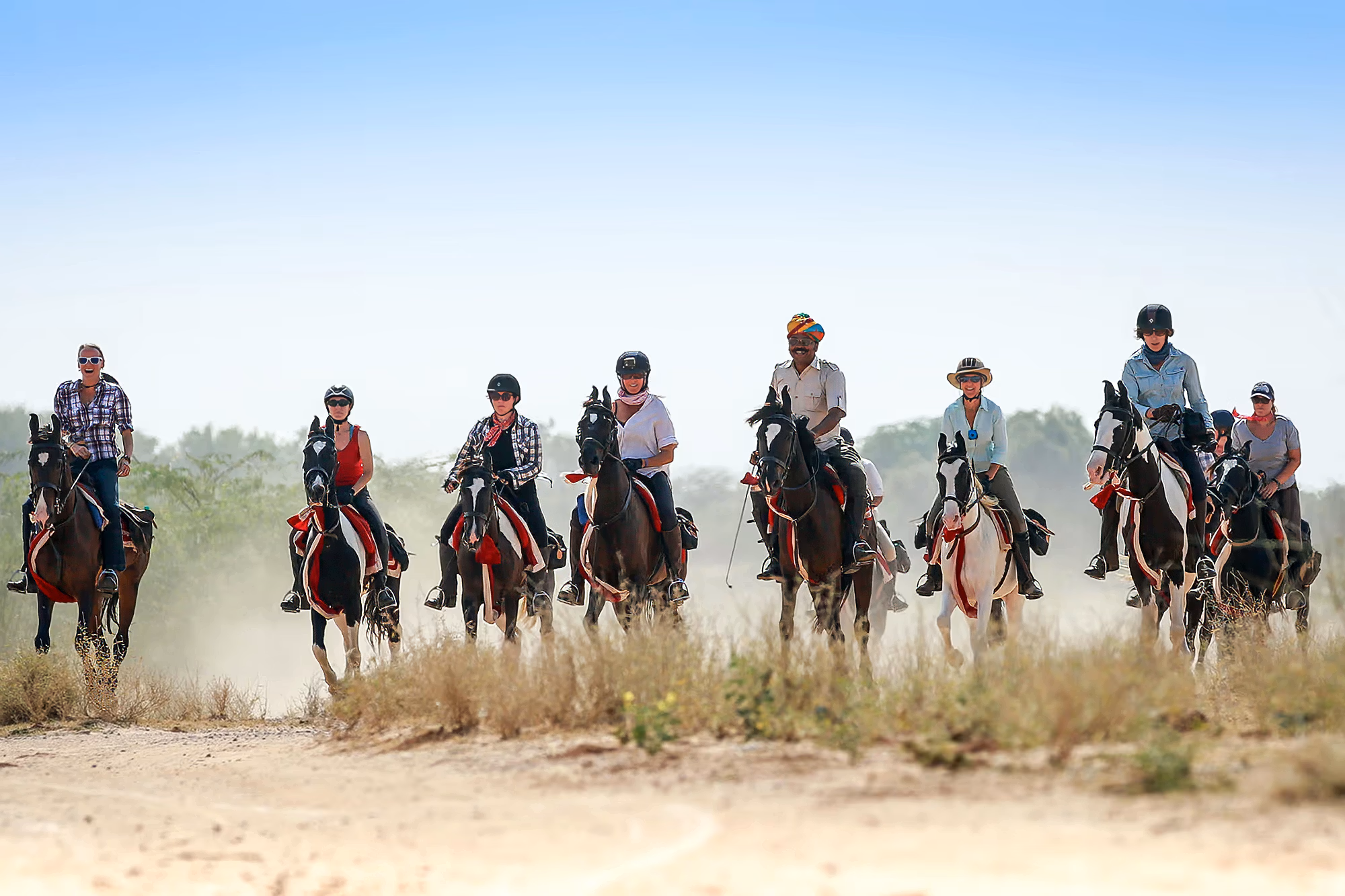 A horse riding tour group rides forward, led by a guide in a traditional turban on an Indian leopard safari.