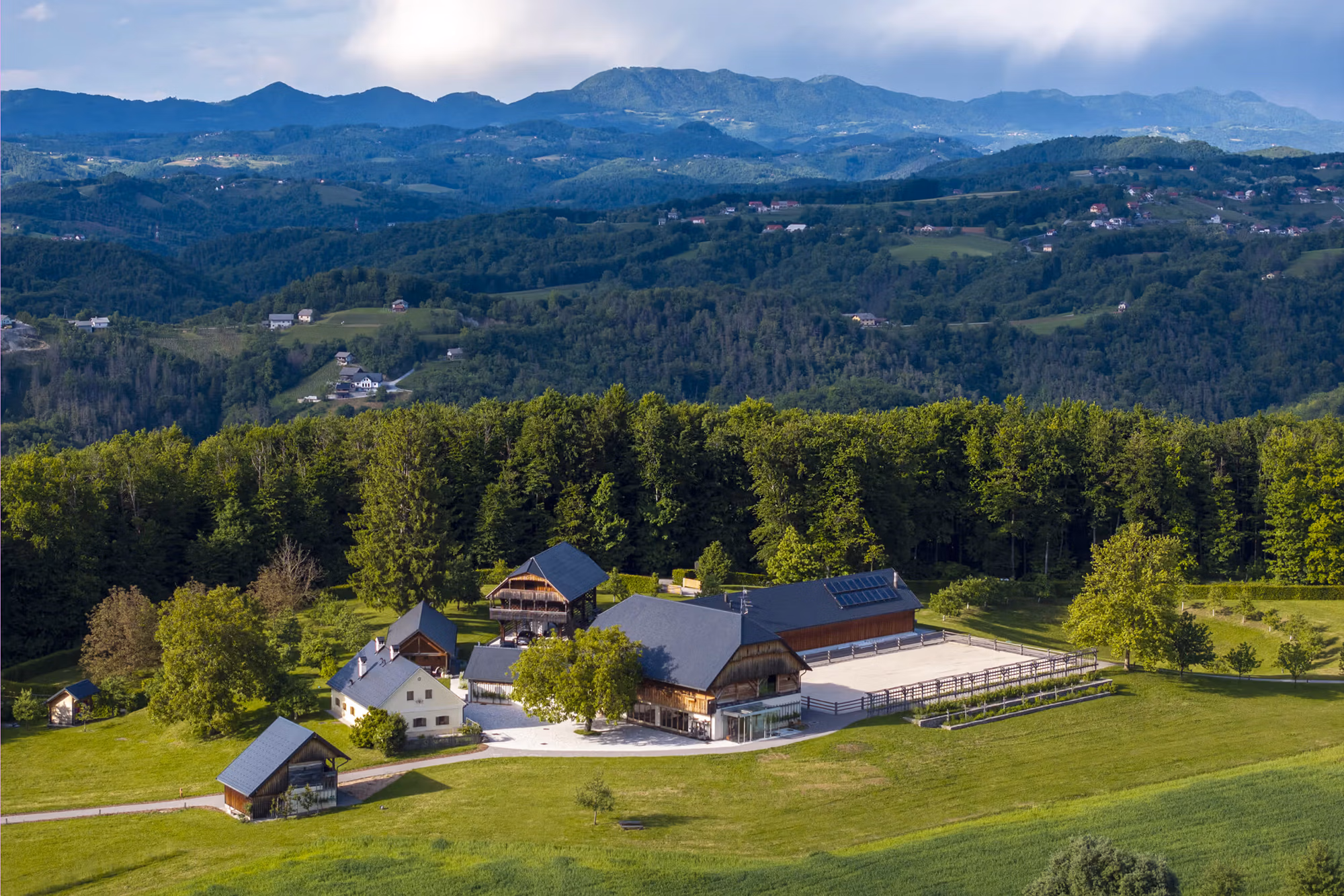 A wide view of a horse range surrounded by lush alpine forests and a dramatic mountain backdrop, the starting point for a multi-day guided horse trail tour in Slovenia.