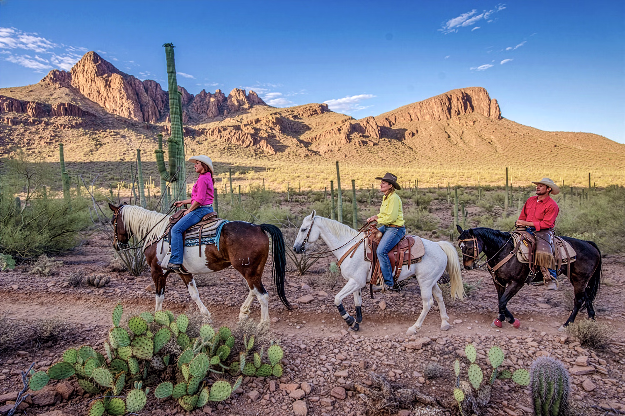 Three riders trot on horseback through a beautiful desert trail,