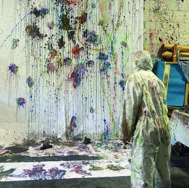 Ein Mensch steht einer Leinwand gegenüber und malt mit Farbe.