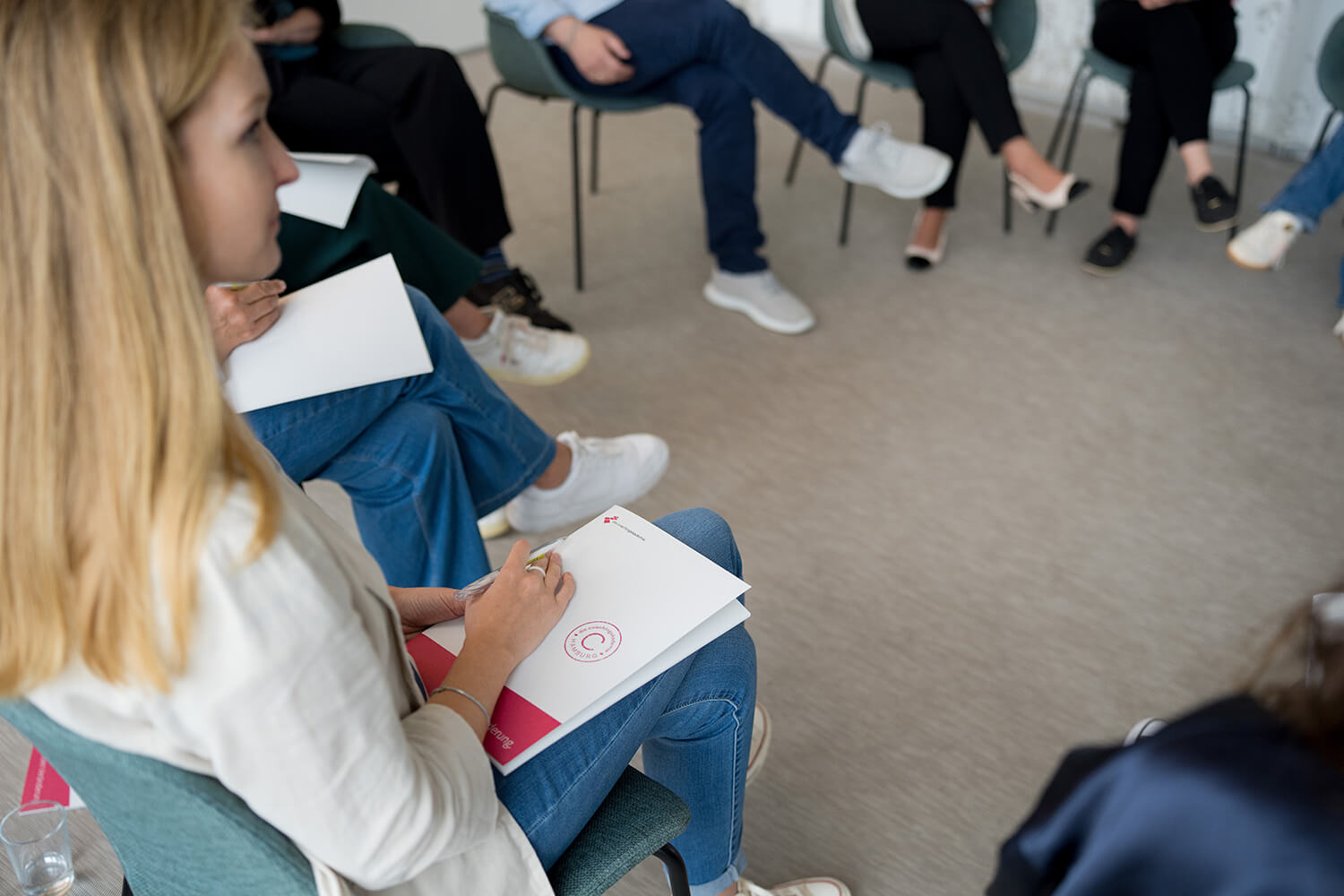 Weiterbildung – Gruppe im Stuhlkreis, Teilnehmende mit Notizblock im Seminarraum